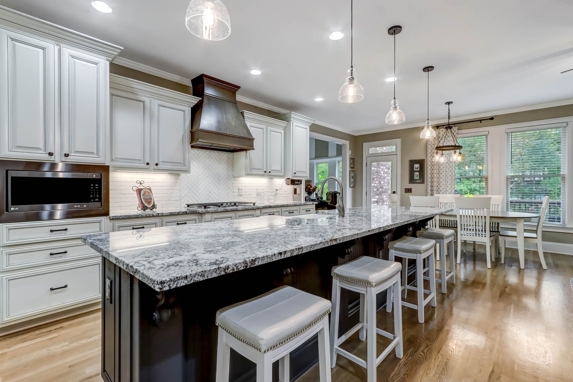 A modern kitchen with white cabinetry, granite countertops, and a dark island with bar stools.