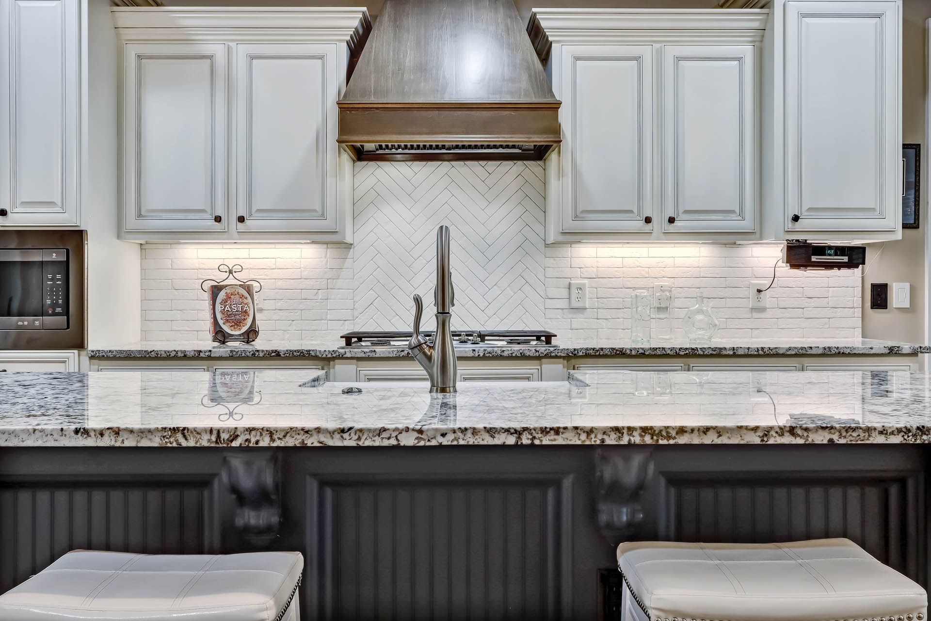 Kitchen with white cabinets, a gray backsplash, and a dark granite countertop. The island features a dark paneling.