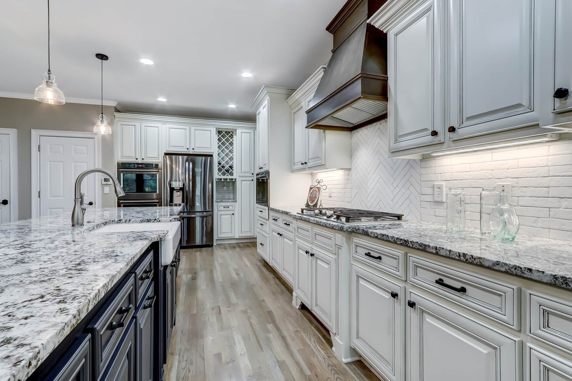 A modern kitchen with white cabinets, stainless steel appliances, and a dark blue island with granite countertops.