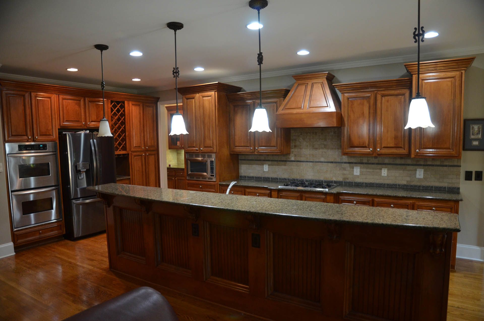 A spacious kitchen with dark wood cabinets and a large island. Stainless steel appliances and pendant lights are featured.