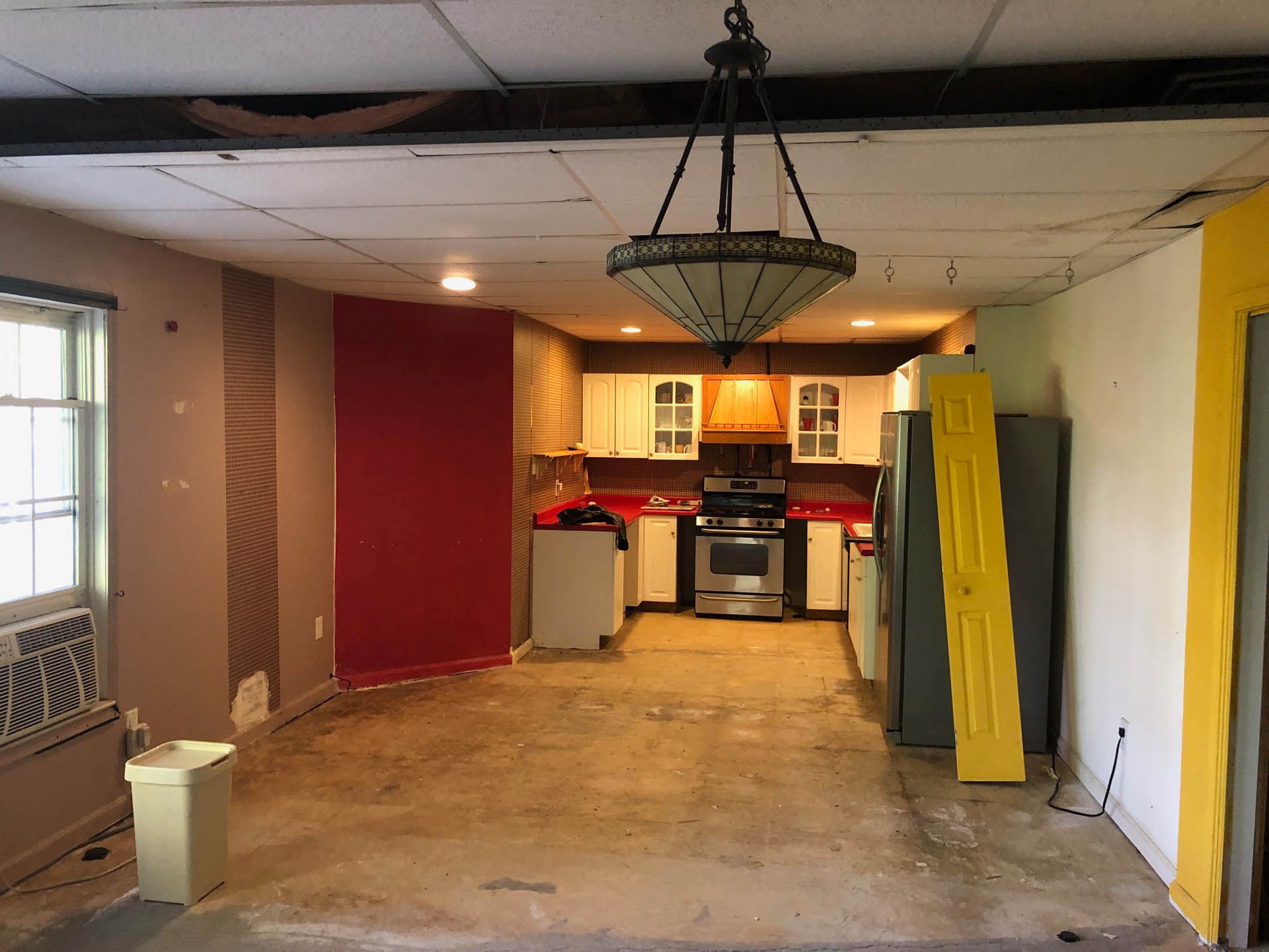 Interior view of a home undergoing renovation; exposed floors, red and yellow walls, and a partly finished kitchen.