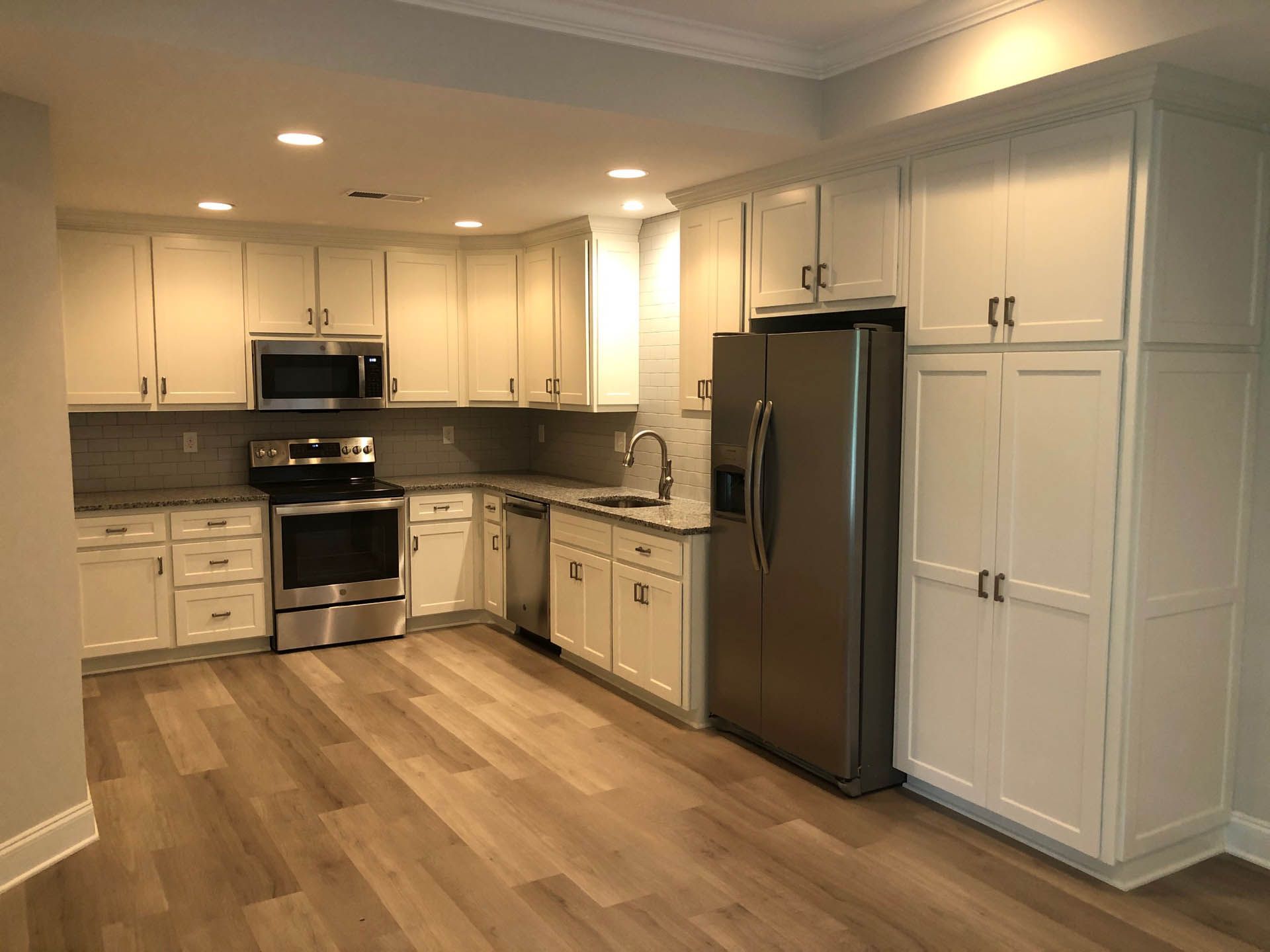 Modern kitchen with white cabinets, stainless steel appliances, granite countertops, and wood-look flooring.