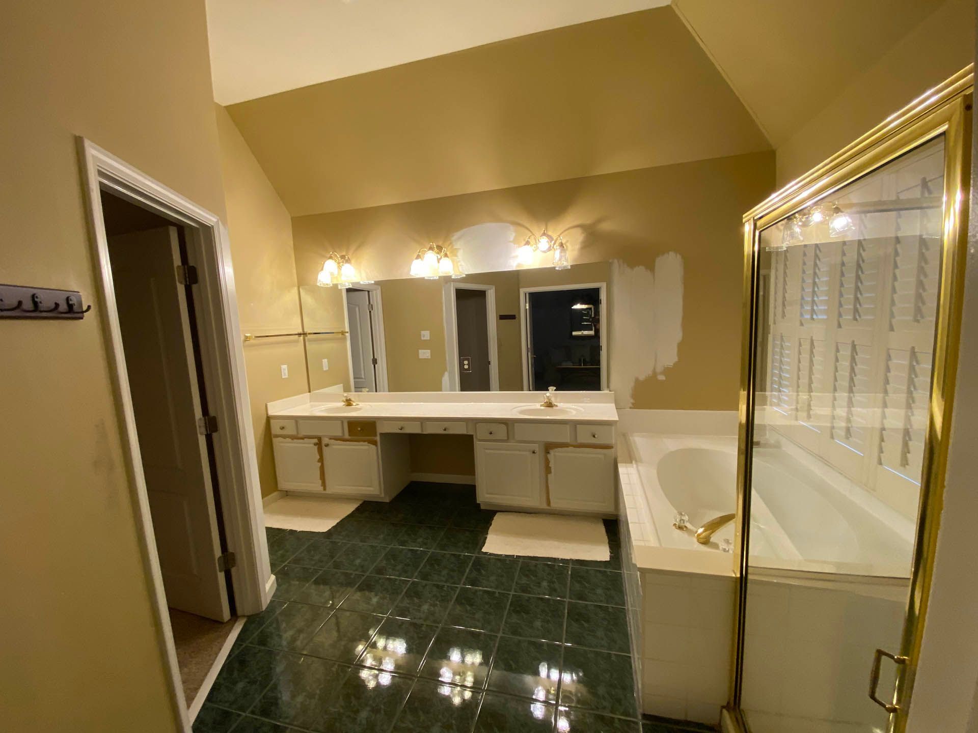 Bathroom with green tiled floor, white vanity, and a golden-framed shower. Walls are painted a pale yellow.