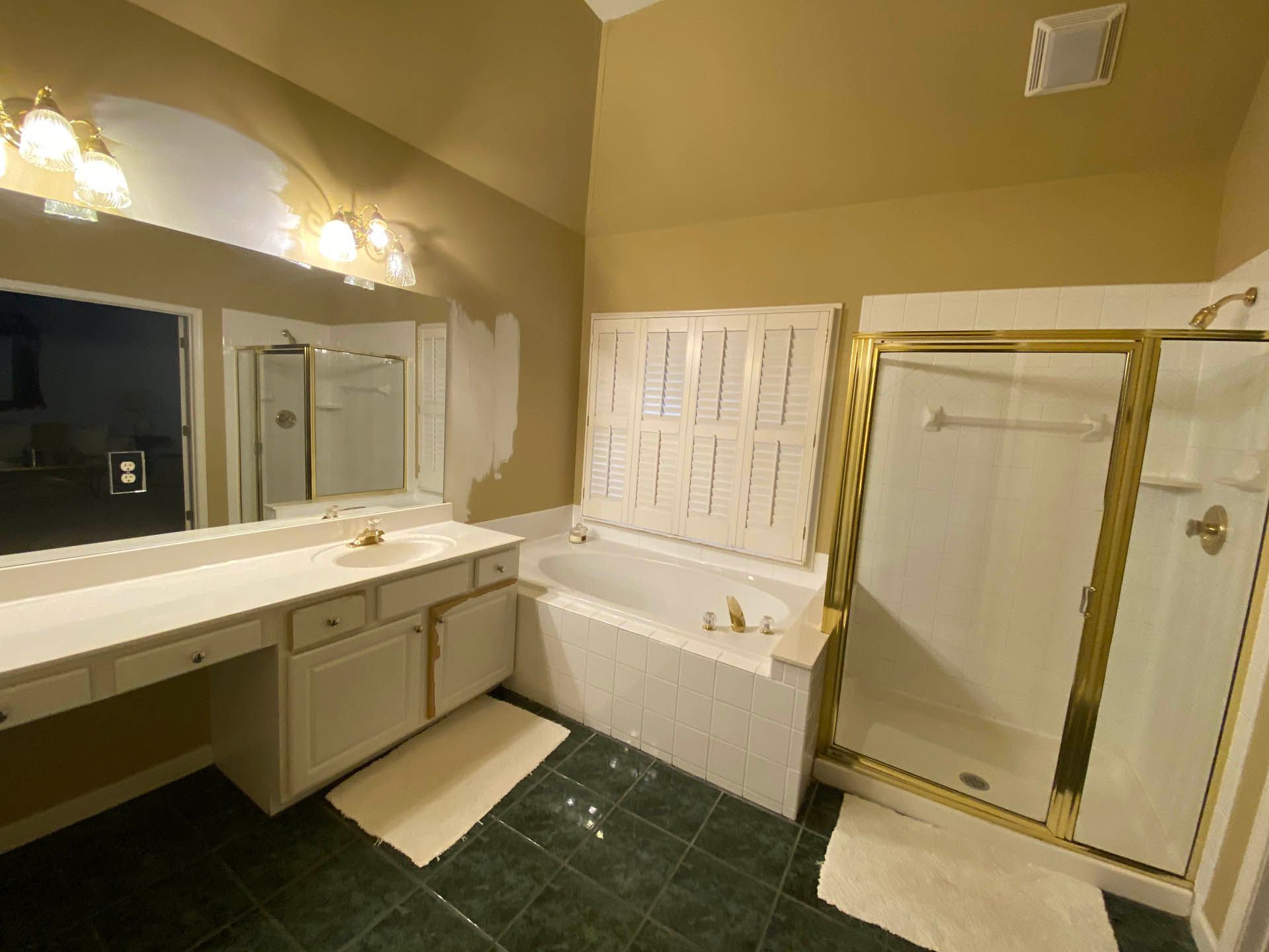 Bathroom with a white vanity, built-in bathtub, and gold-framed shower. Green tiled floor, yellow walls, and bright lighting.