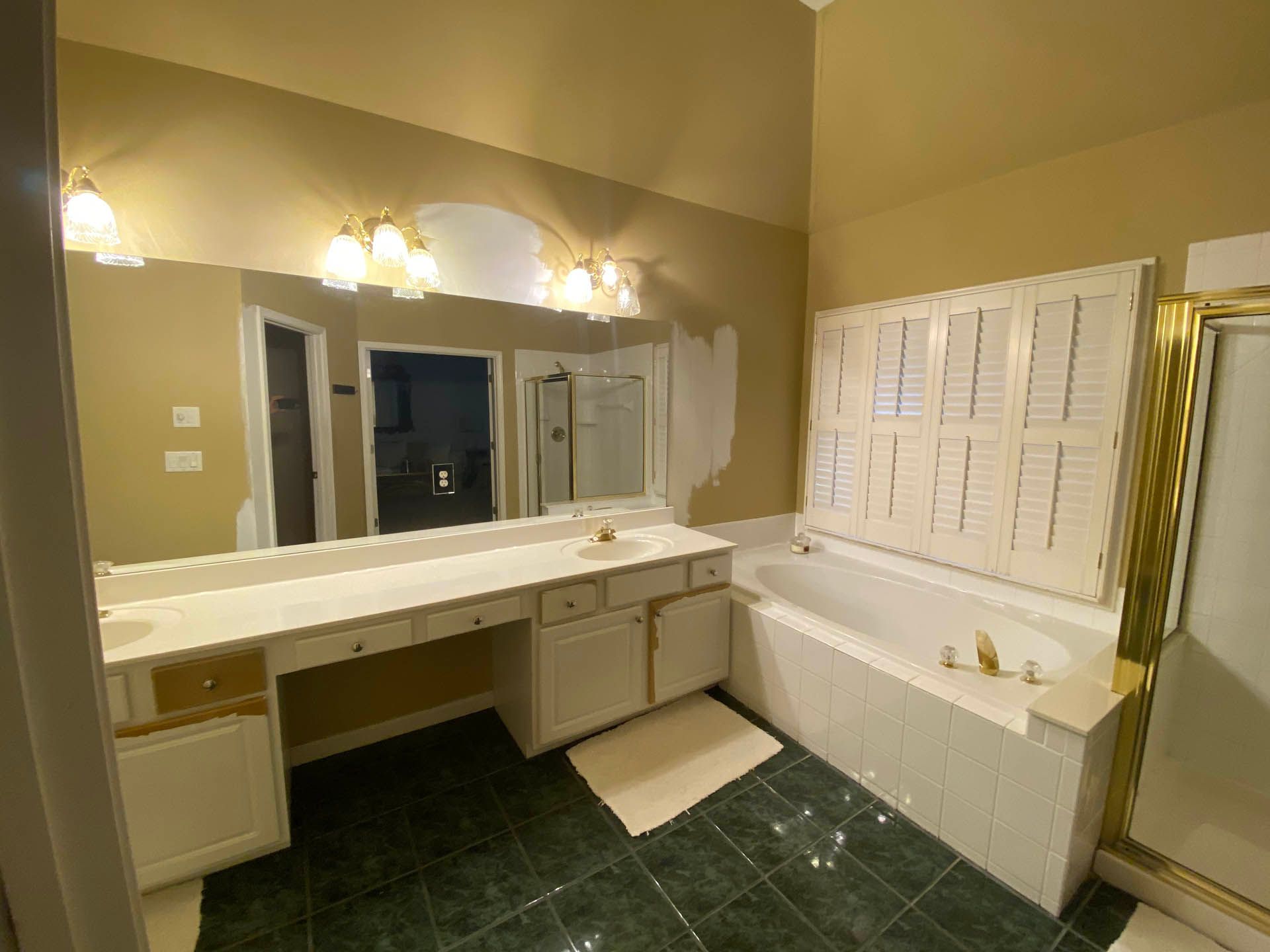Bathroom with white vanity, bathtub, and shutters; green tiled floor, gold trim.