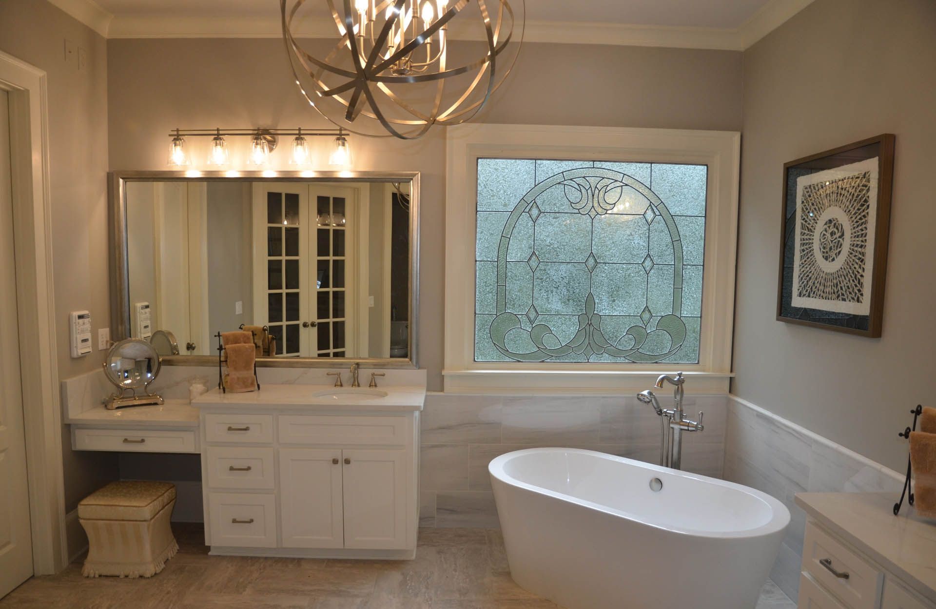 Bathroom with white vanity, tub, and window. Features a large mirror and a decorative chandelier.