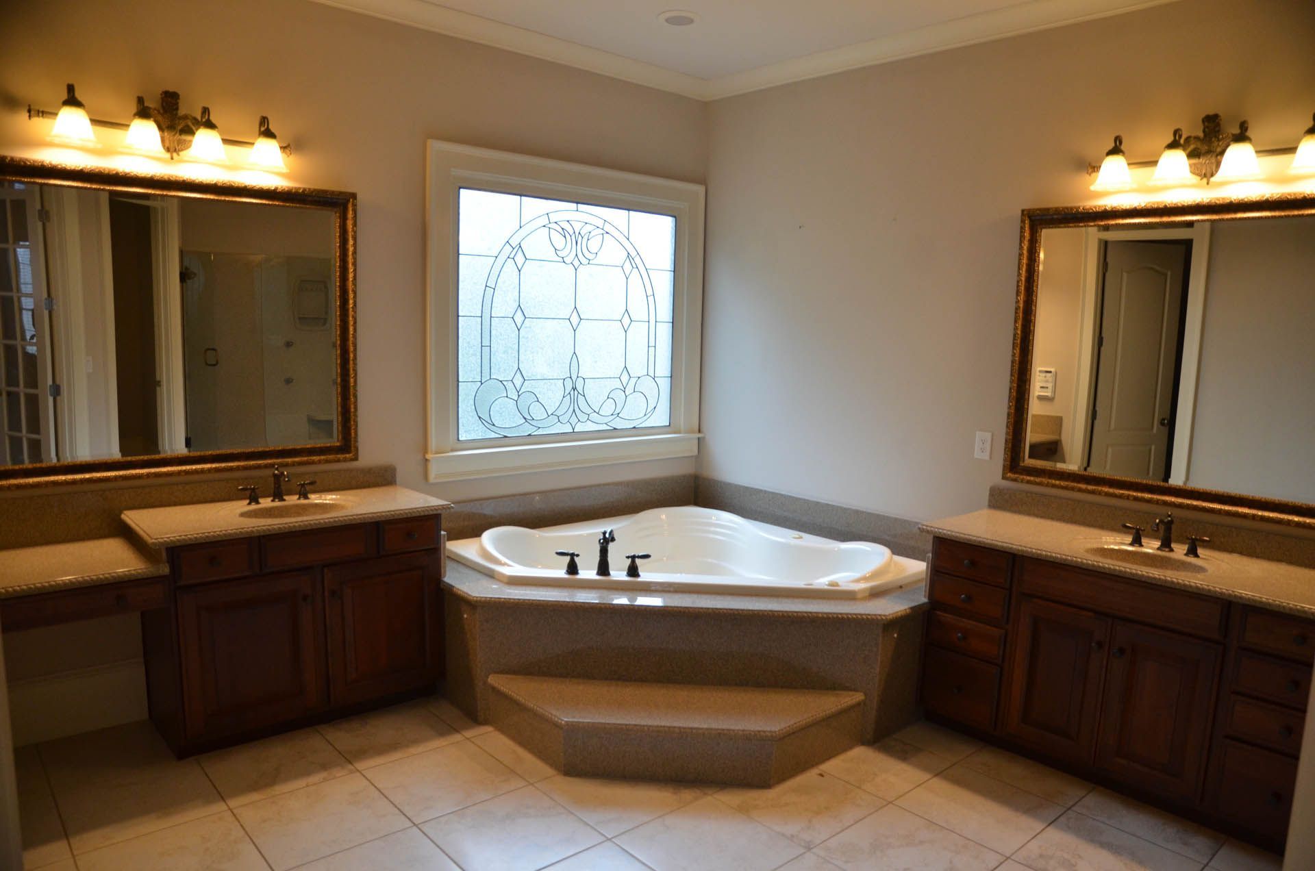 Bathroom with two vanities flanking a corner bathtub. Neutral color scheme with dark wood cabinets and light-colored tile.