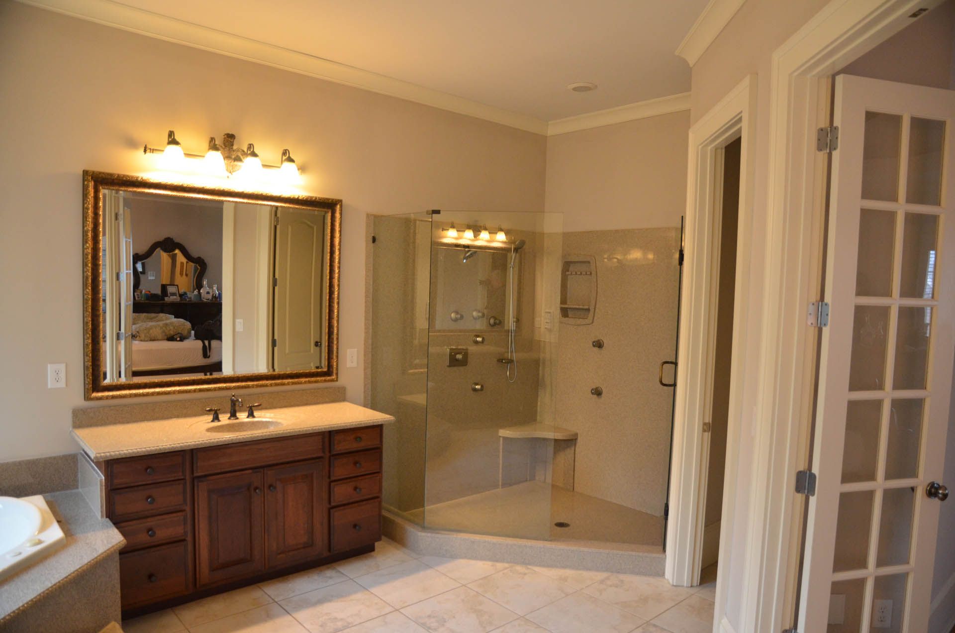 A spacious bathroom with a dark wood vanity, large mirror, and glass shower; cream-colored walls and tile.