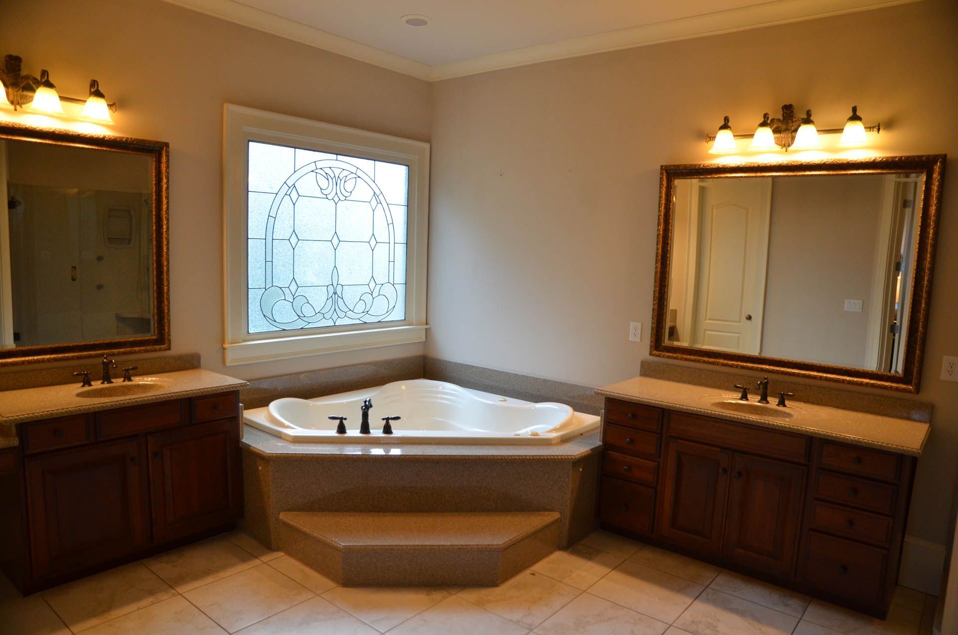 Bathroom with a corner jacuzzi tub, flanked by two vanities with mirrors and lighting fixtures.