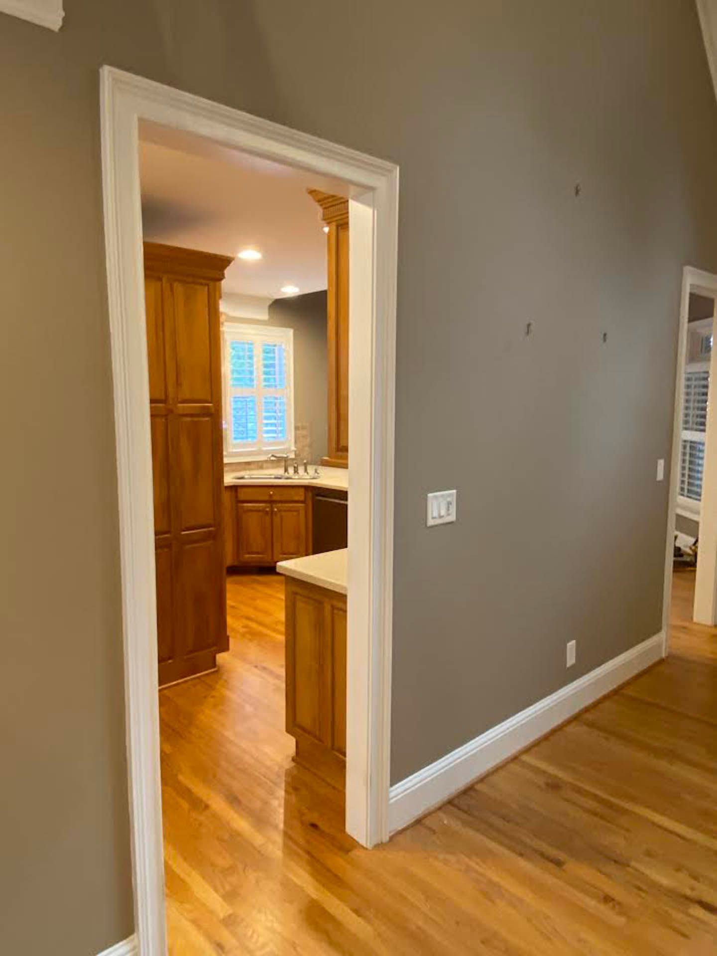 A doorway leading to a kitchen with wooden cabinets, seen from a room with wood floors and a neutral-colored wall.
