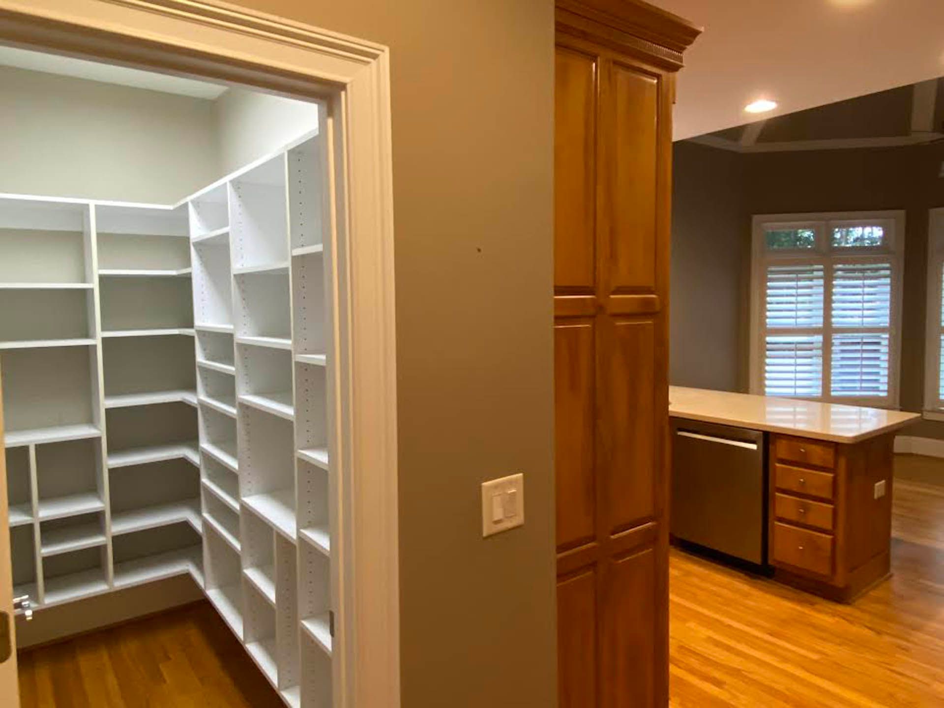 A kitchen with a pantry entrance on the left, built-in shelves, and wooden cabinets and island with a dishwasher and drawers.