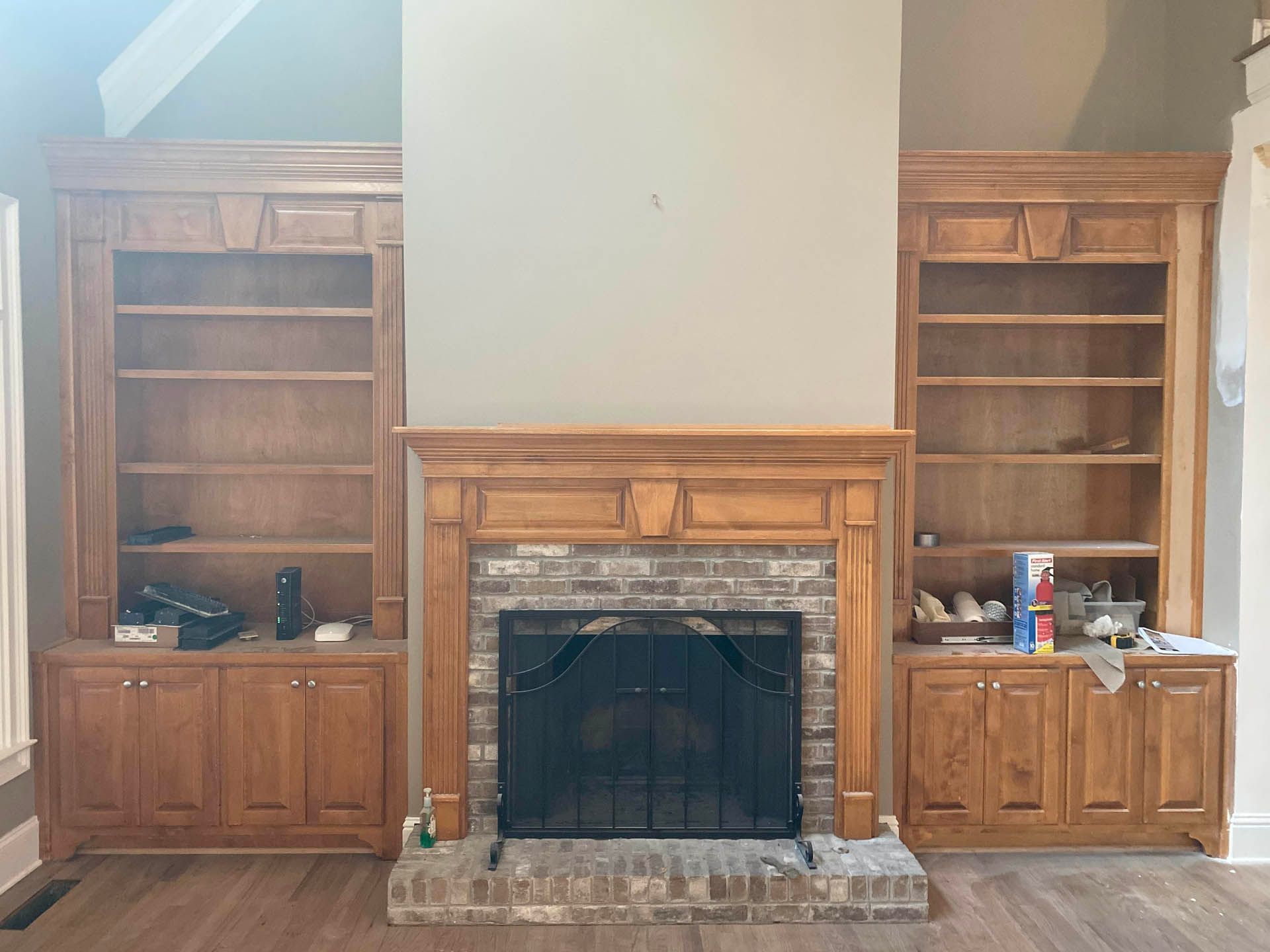 Wooden bookshelves flank a brick fireplace with a black screen. The setup is in a room with light-colored walls and hardwood floors.