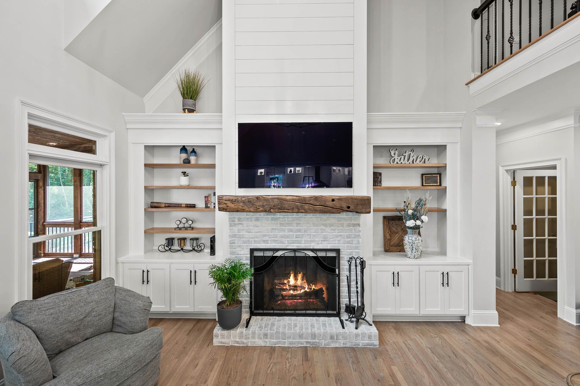 Cozy living room with white fireplace, built-in shelves, and a TV above the fireplace. A gray sofa and a small plant sit in front.