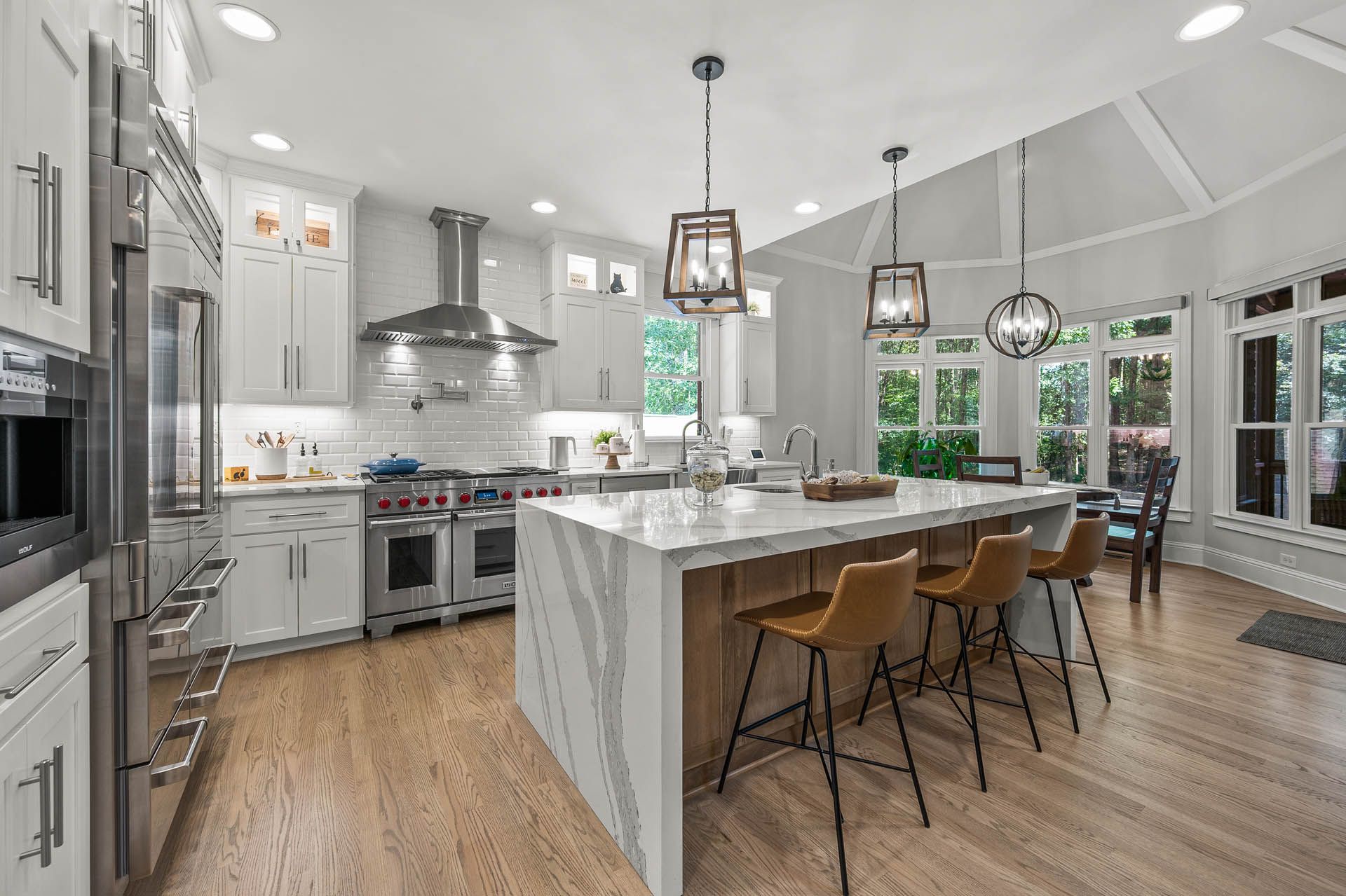 Spacious, bright kitchen with a large island, stainless steel appliances, white cabinets, and wooden floors.  Bar stools line the island, and pendant lights hang overhead.