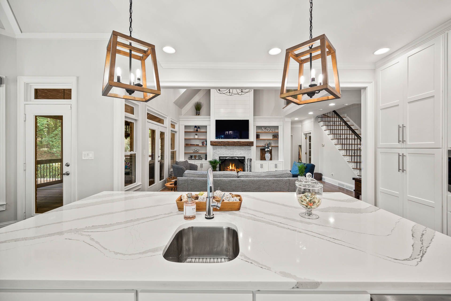 Bright, open-concept kitchen with a large island and view into the living room, featuring wooden pendant lights, white cabinetry, and a stone countertop.
