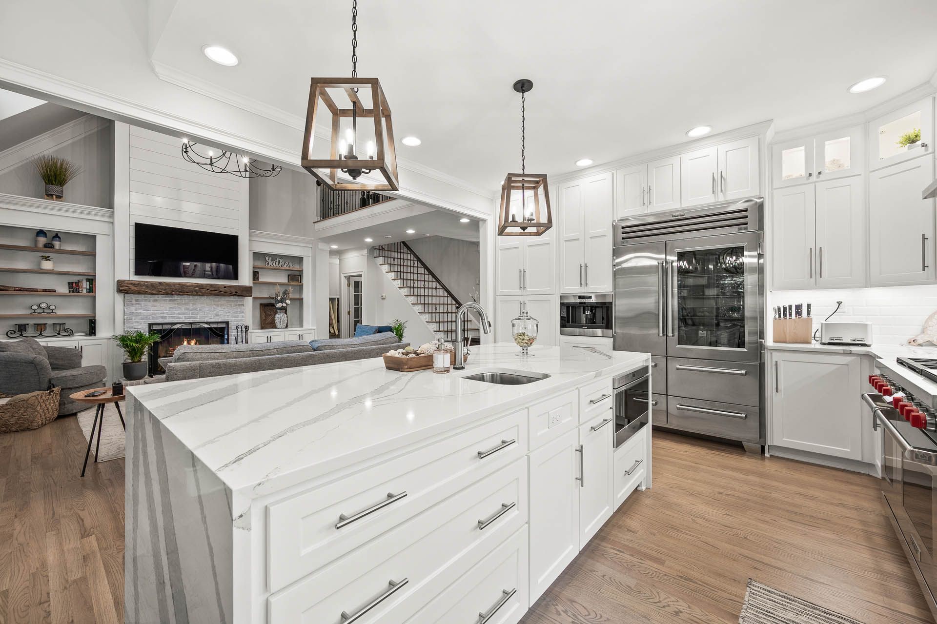 Spacious, white kitchen with large island, stainless steel appliances, and open layout into living area with fireplace.