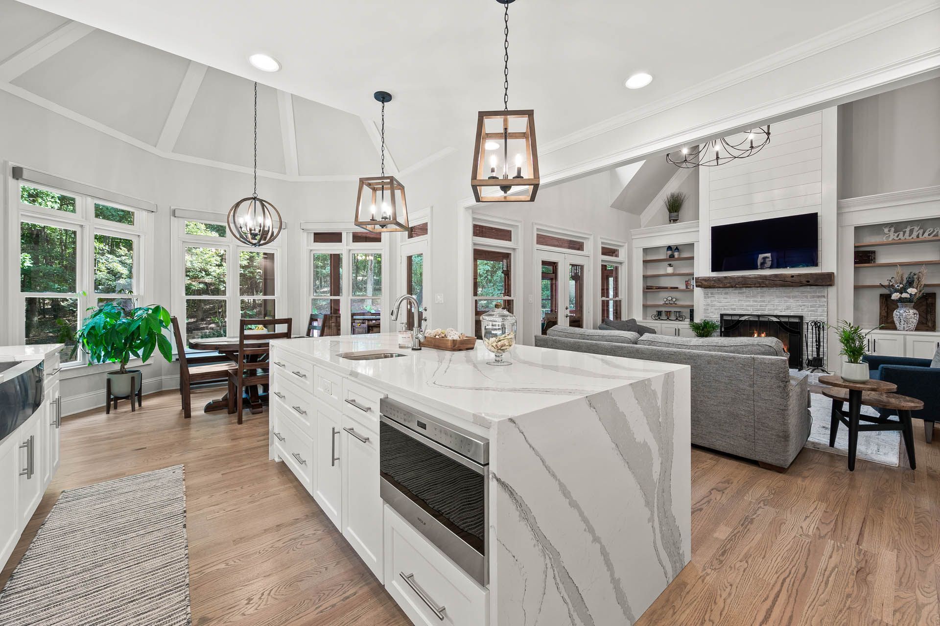 Spacious, modern kitchen with white cabinets, marble island, and open to a living area with a fireplace and television.