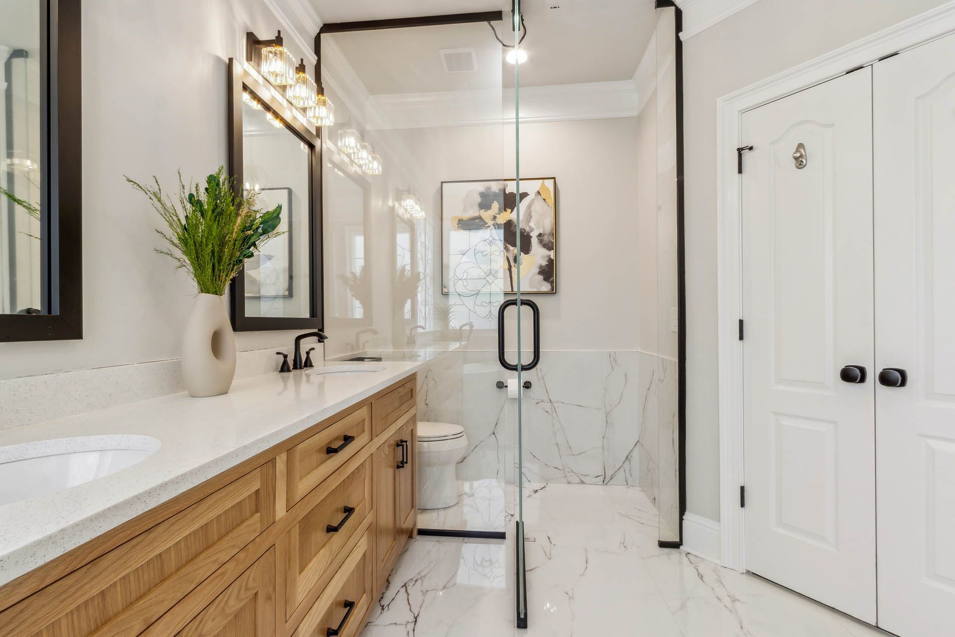 A modern bathroom with light wood vanity, glass shower, and white marble tile. Black accents on the mirror frames and door hardware.