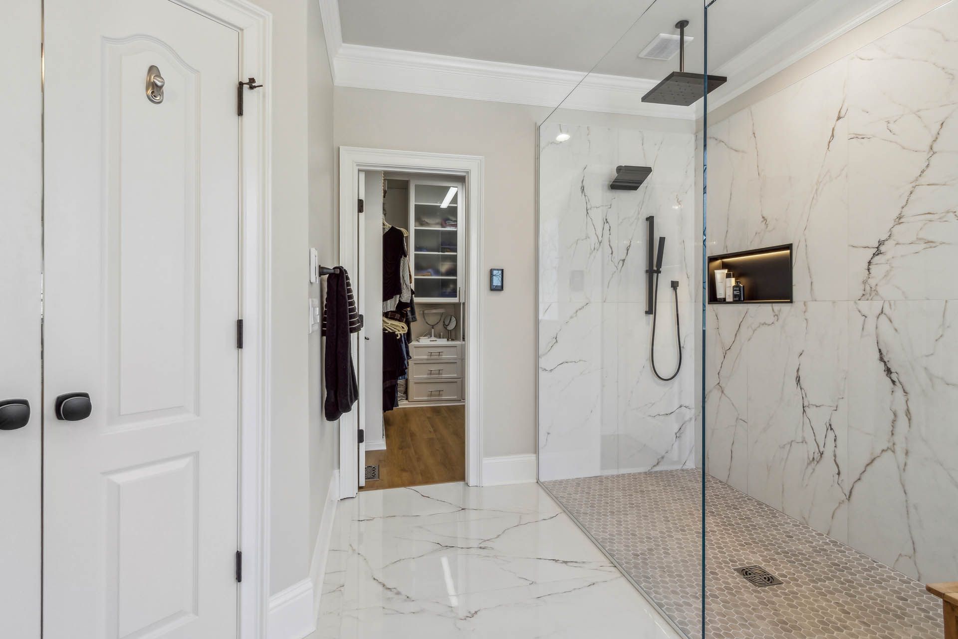 Bathroom with a large marble-tiled shower, open walk-in closet, and white doors. The floor is marble-like tiles.