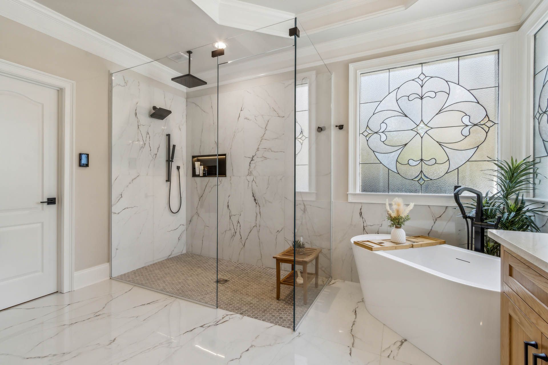 Spacious bathroom with a walk-in shower, freestanding tub, and decorative stained glass window. Marble-like tile flooring and walls, wood accents.