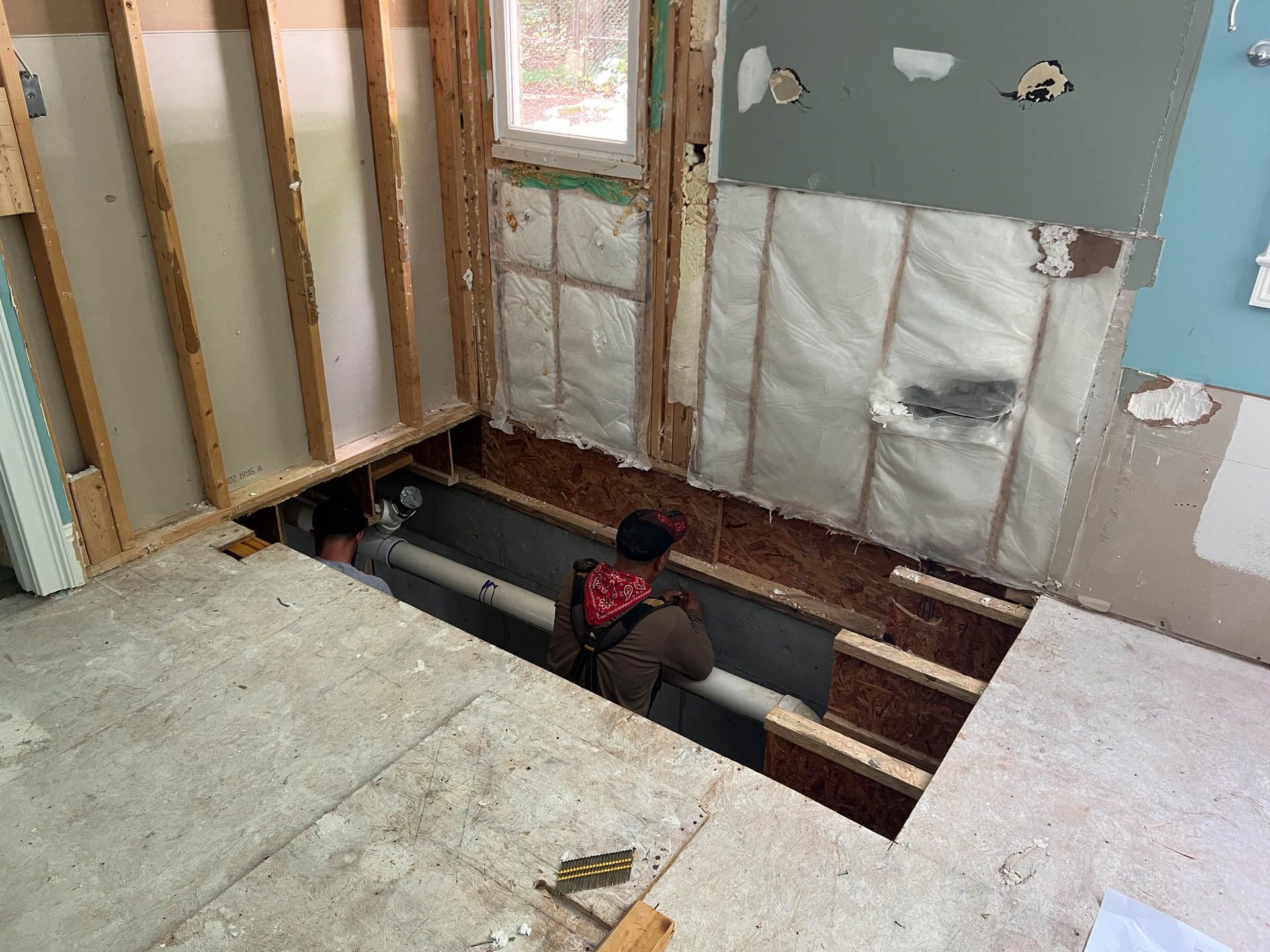Construction worker in a bathroom, installing plumbing. The space is under renovation, with exposed walls and insulation.