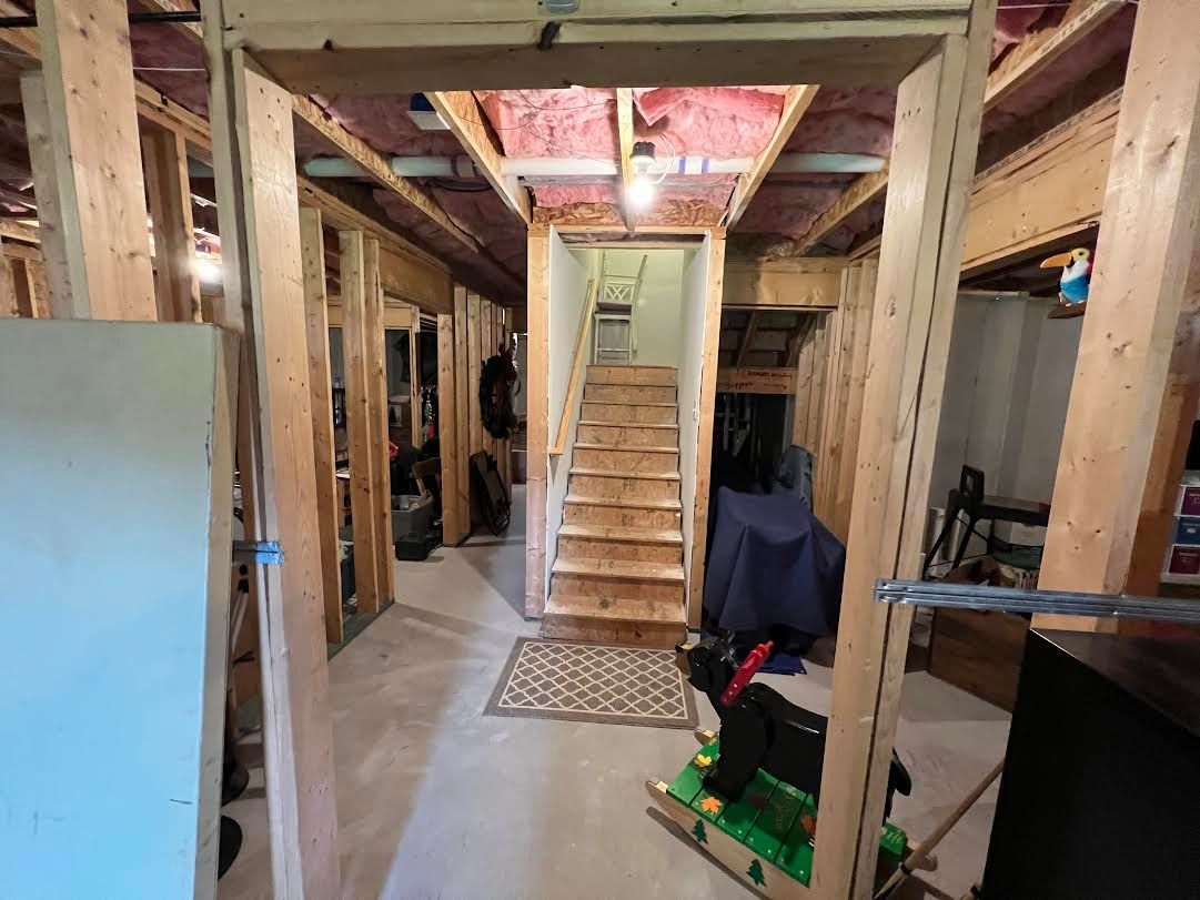 Interior view of a basement hallway under construction, with wooden framing, stairs, and an open doorway.