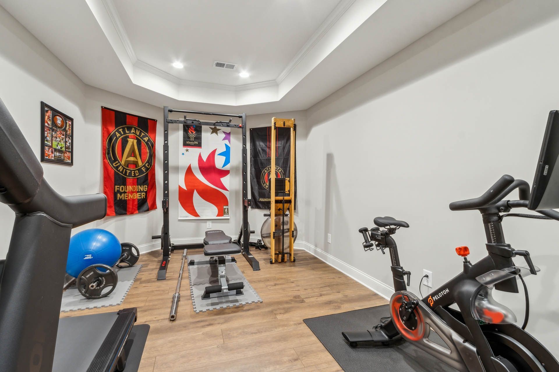 Home gym with fitness equipment, including a treadmill, stationary bike, weights, and weight bench. Flags hang on the wall.