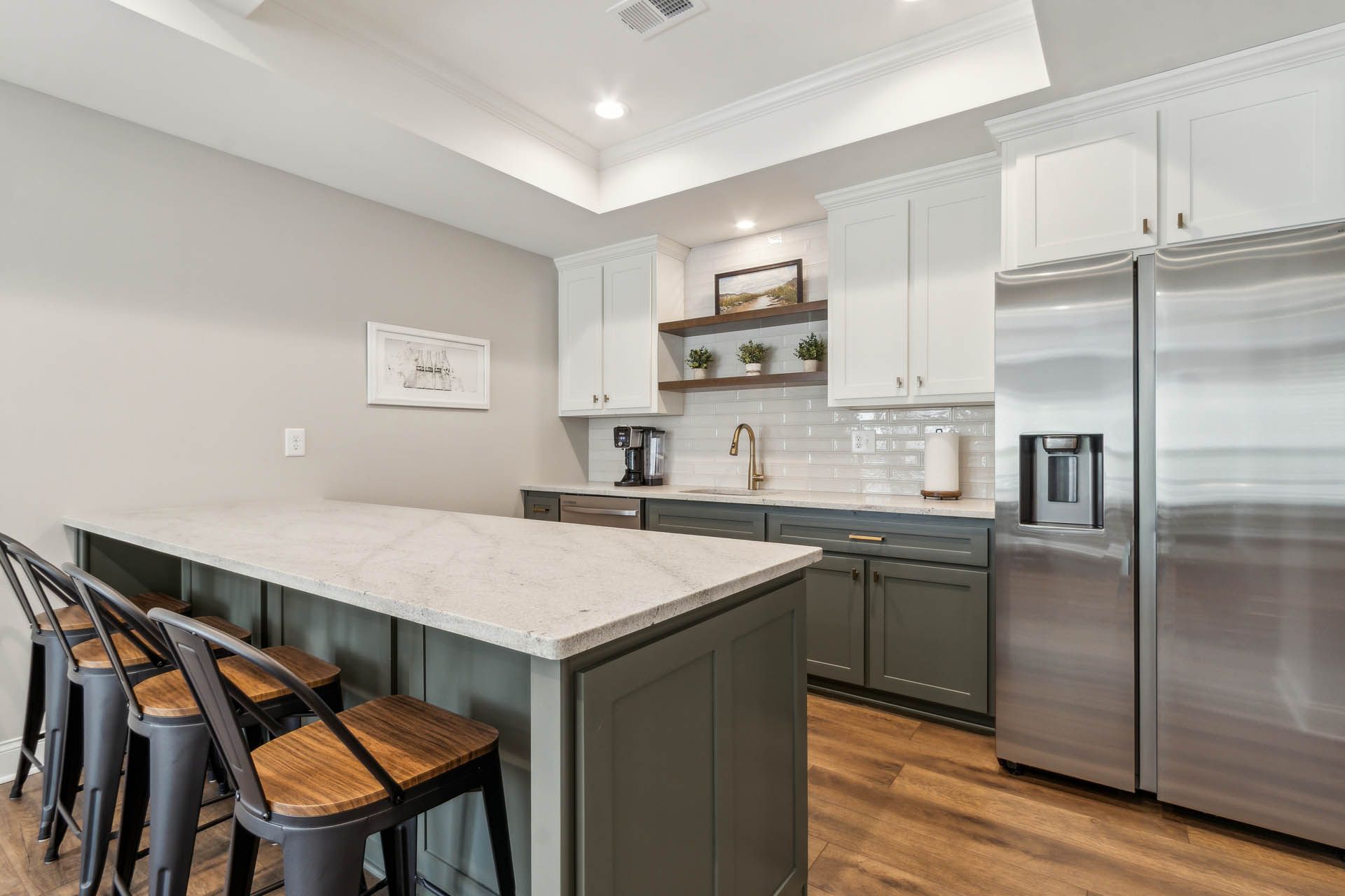 Modern kitchen with white countertops, olive green cabinets, stainless steel refrigerator, and island with bar stools.