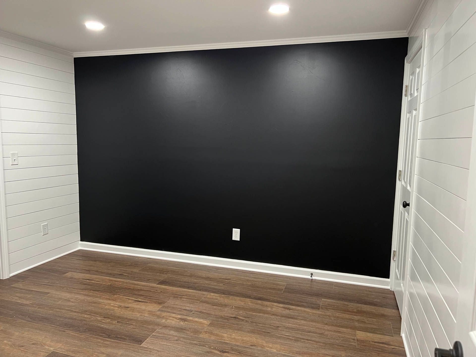 A room with a dark black accent wall. The other walls are white with horizontal planking. Wooden floors.