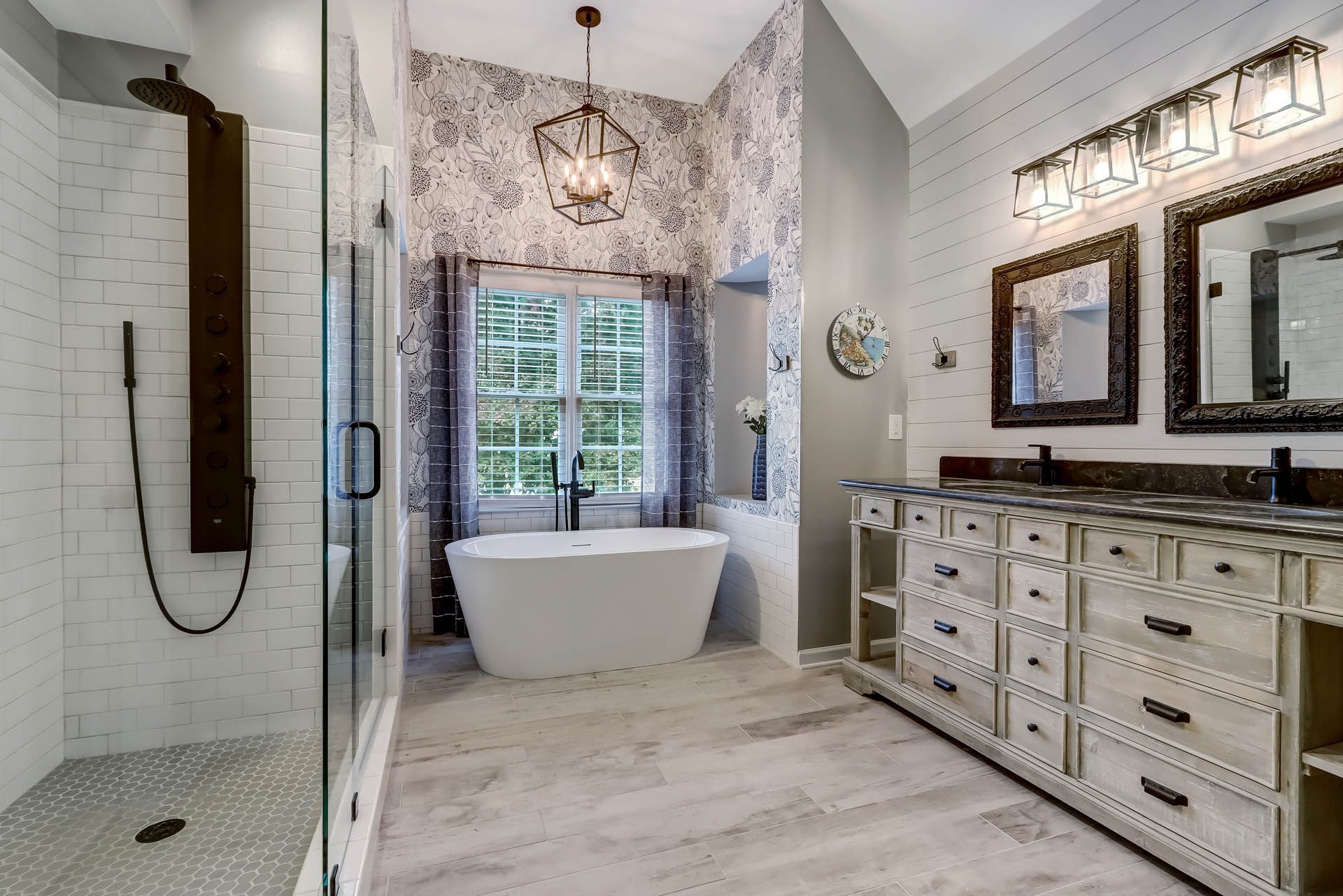 Spacious, white bathroom with a freestanding tub in front of a window, a large shower, and a double vanity.