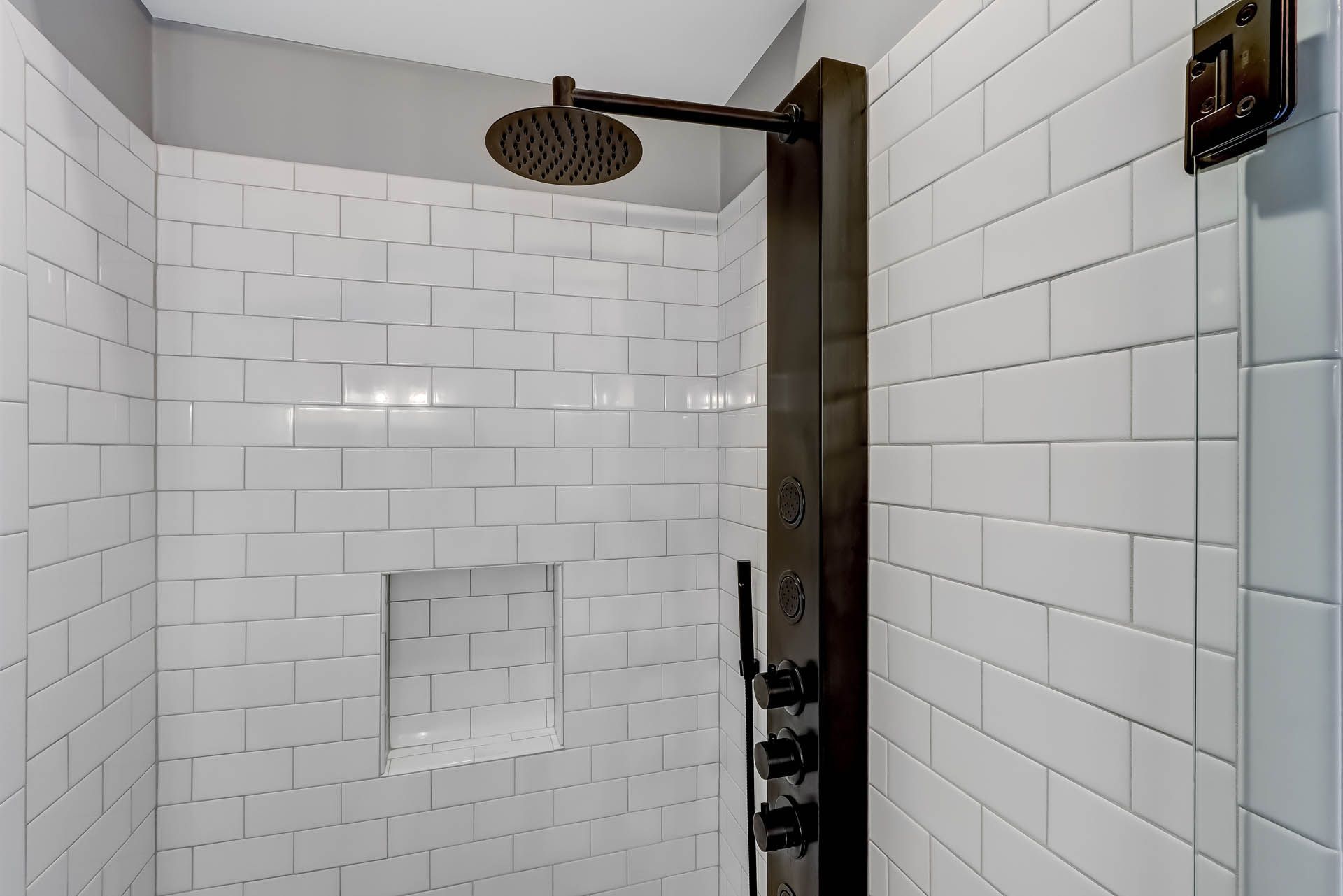 a shower with white tiles and a black shower head