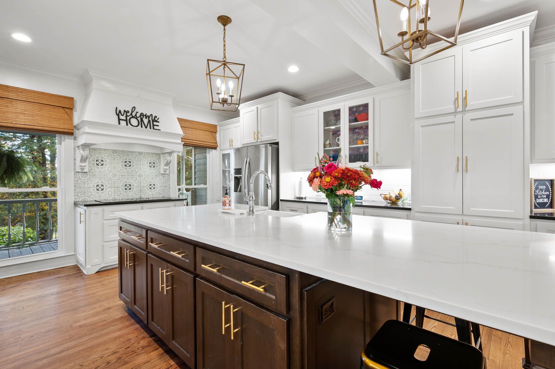 A modern kitchen with a large island. White countertops, dark cabinets, and gold hardware contrast with the white upper cabinets and island.