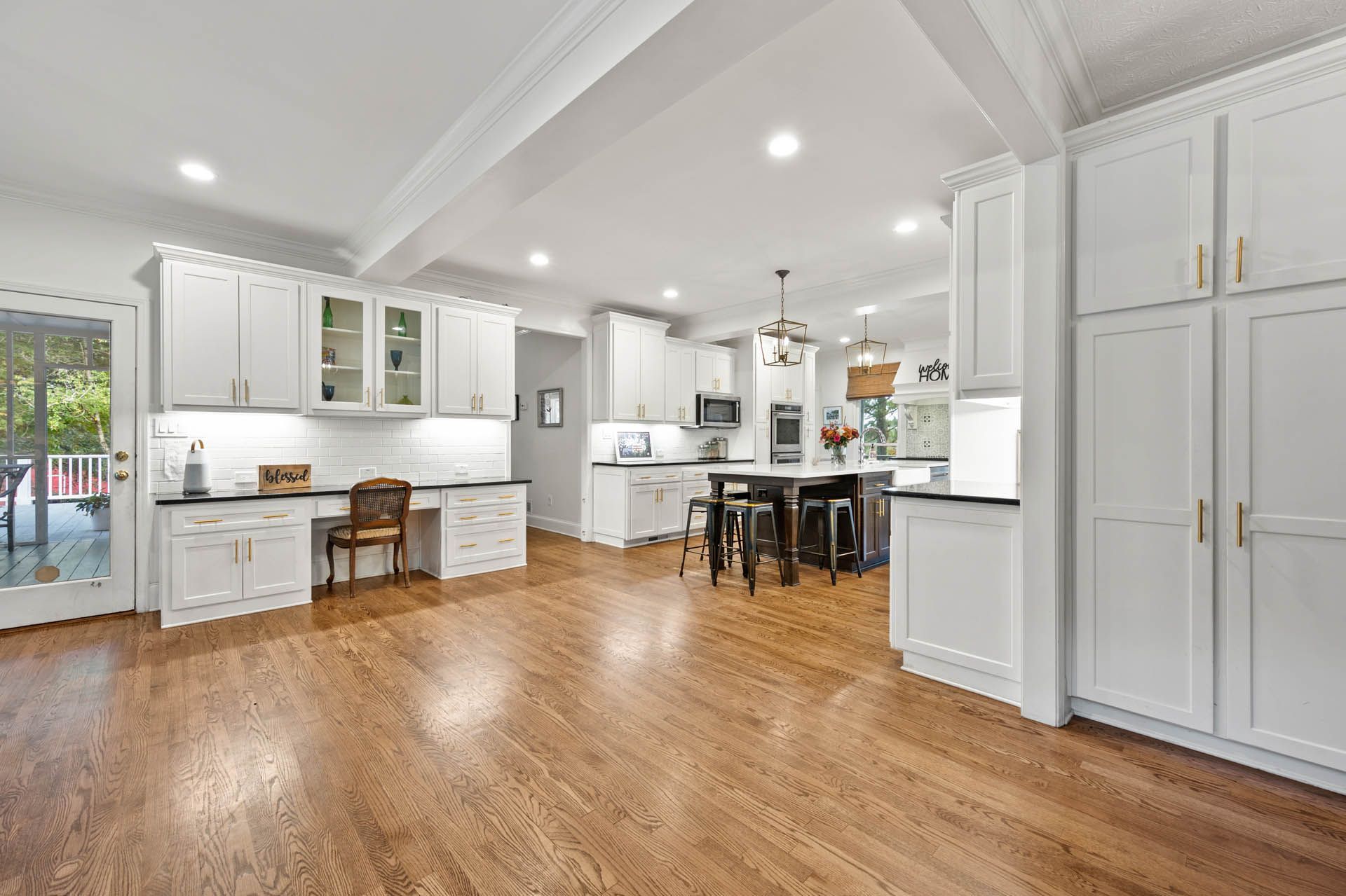 Spacious white kitchen with hardwood floors, a desk area, and a large island with stools.