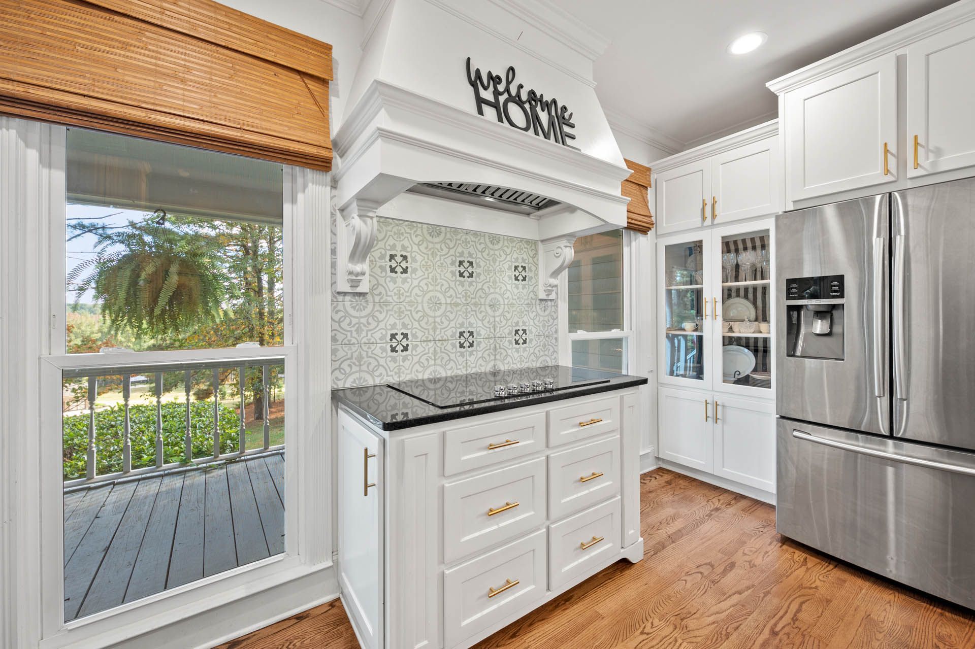 White kitchen with an island stove, stainless steel refrigerator, and a window overlooking a porch.