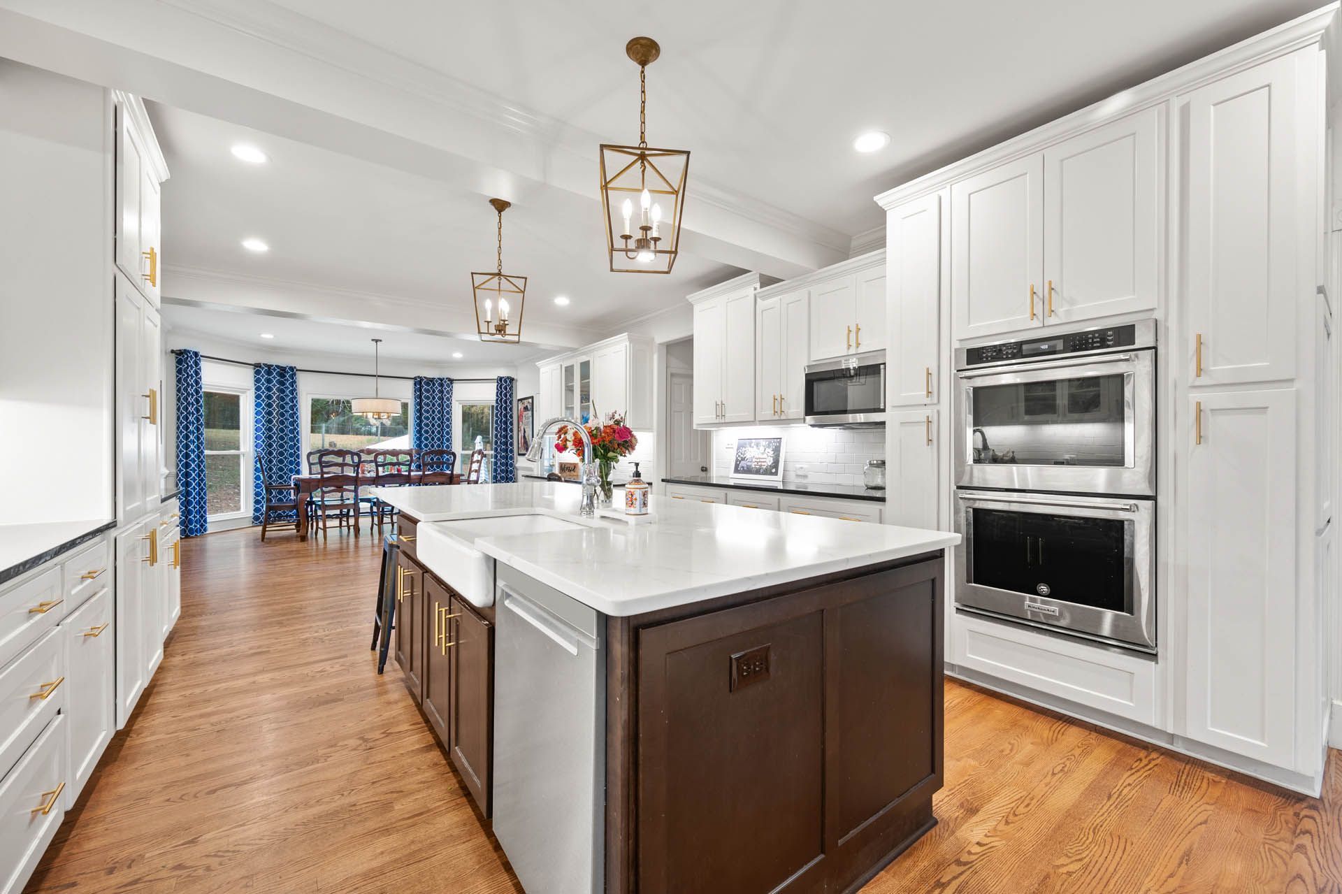 Spacious, bright kitchen with white cabinets, dark brown island, and stainless steel appliances. Hardwood floors and pendant lights.