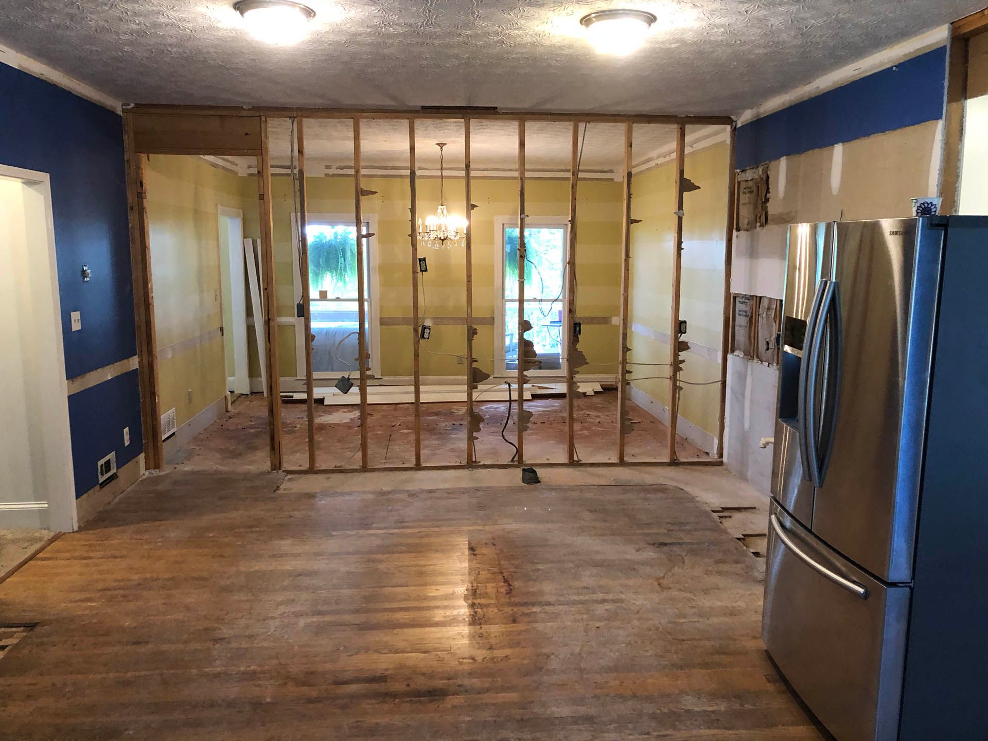 Renovated interior: demolition of a wall between two rooms. Exposed wooden studs, distressed wood floor, and blue painted walls.