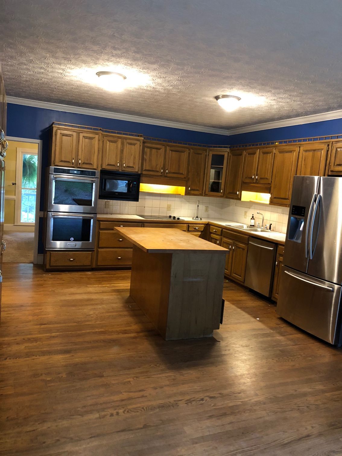 Spacious kitchen with wooden cabinets, island, stainless steel appliances, and hardwood floors. Blue upper walls and white ceiling trim.
