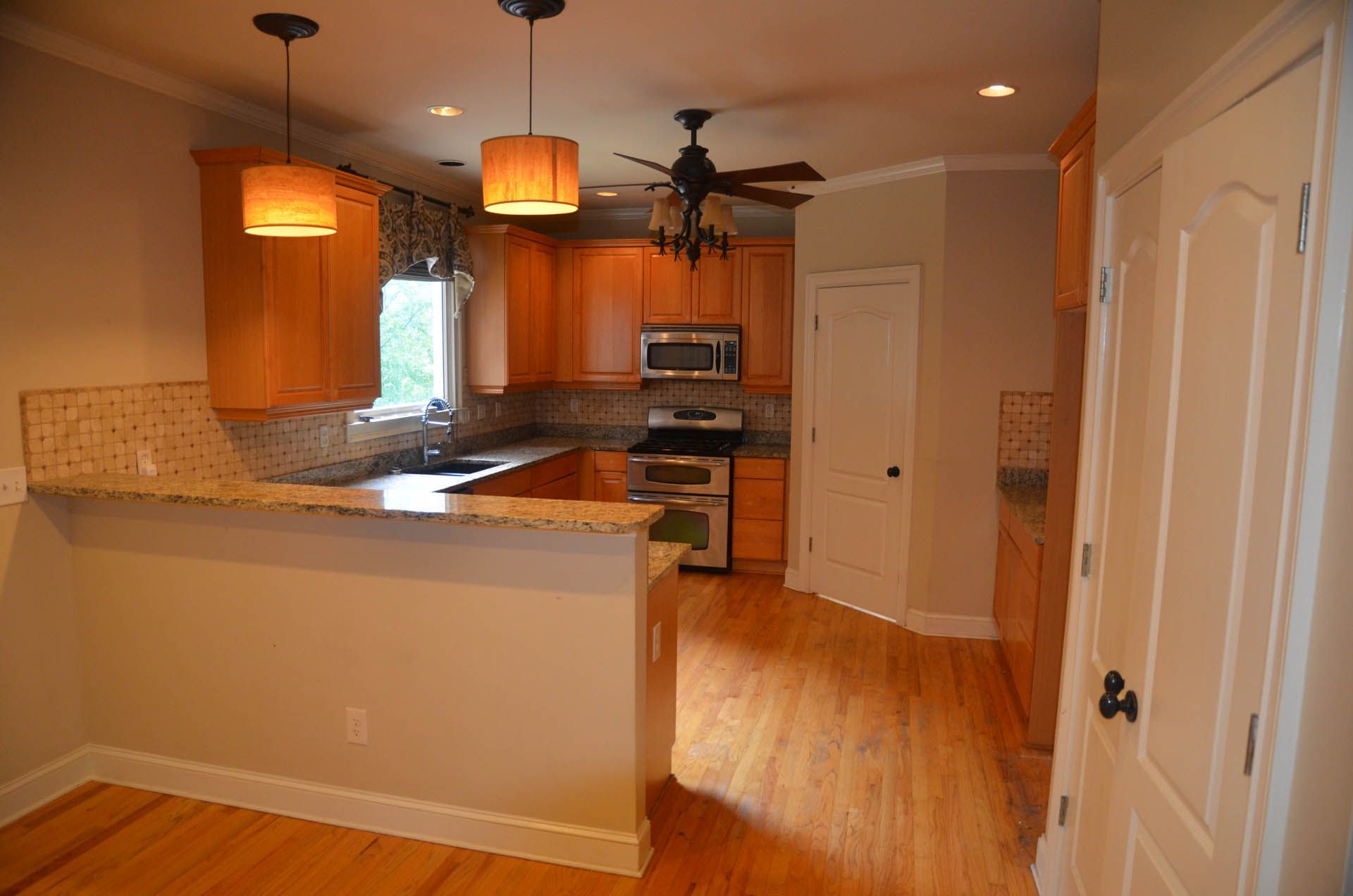 Kitchen with wood cabinets, granite countertops, and hardwood floors. Features a breakfast bar, stainless steel appliances, and two pendant lights.
