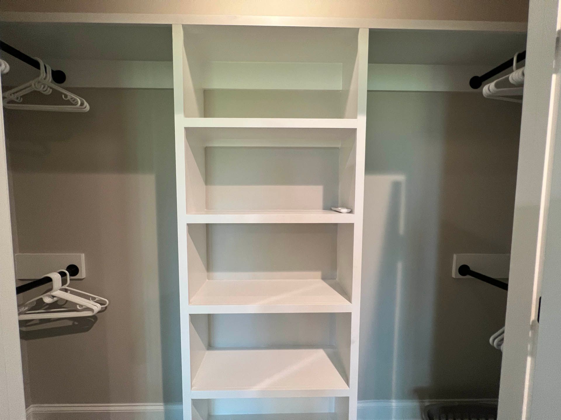 Empty white closet interior with shelves in the center, hanging rods on the sides, and light gray walls.
