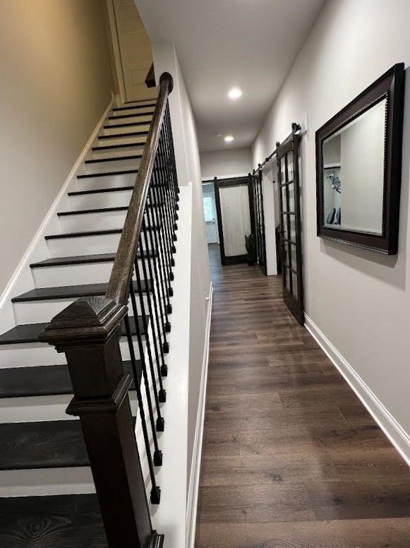 Hallway with dark wood floor, stairs on left, and doors and a mirror on the right. Walls are neutral colors.