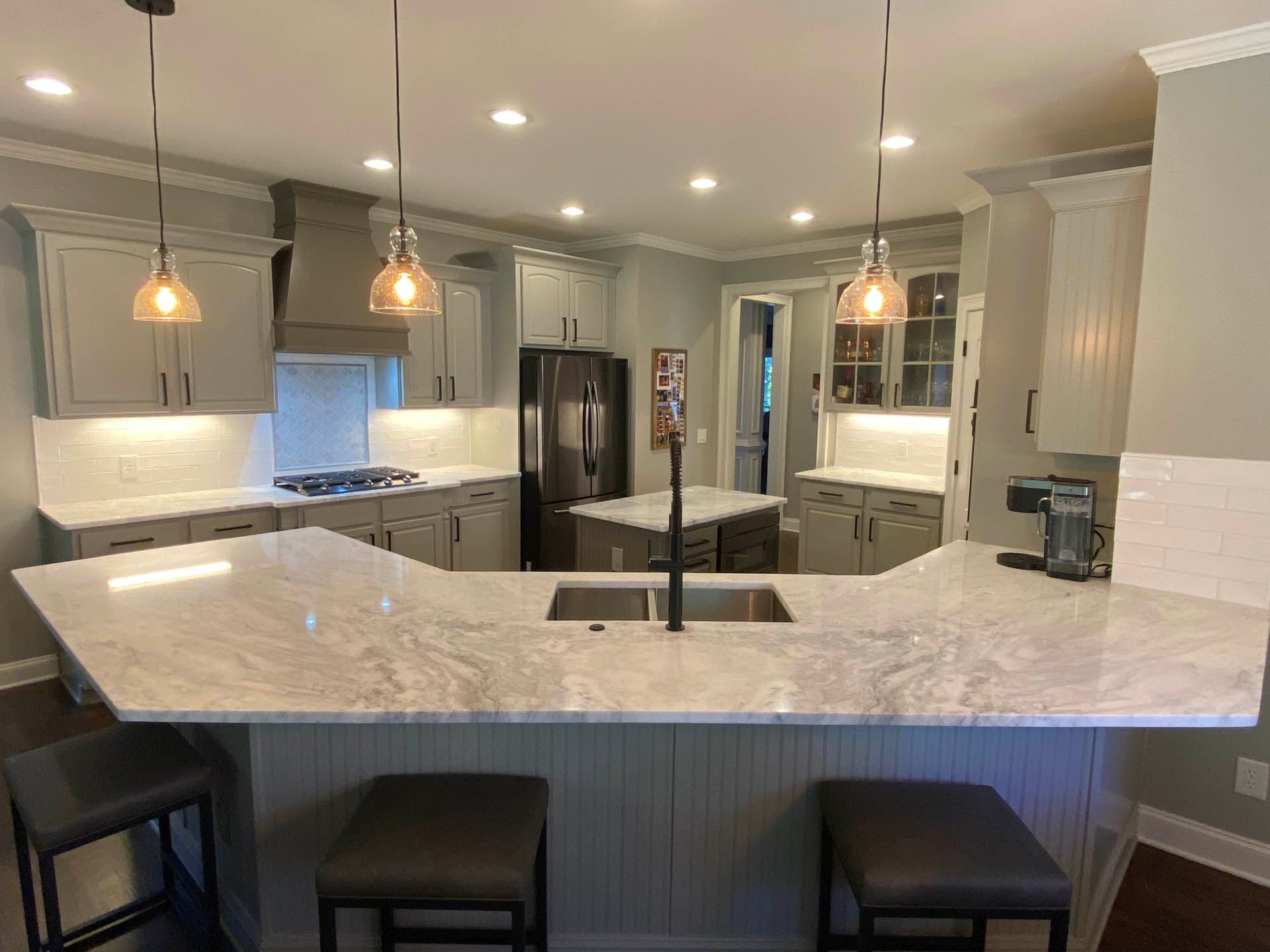 A modern kitchen with light gray cabinets, a white countertop, and three pendant lights.