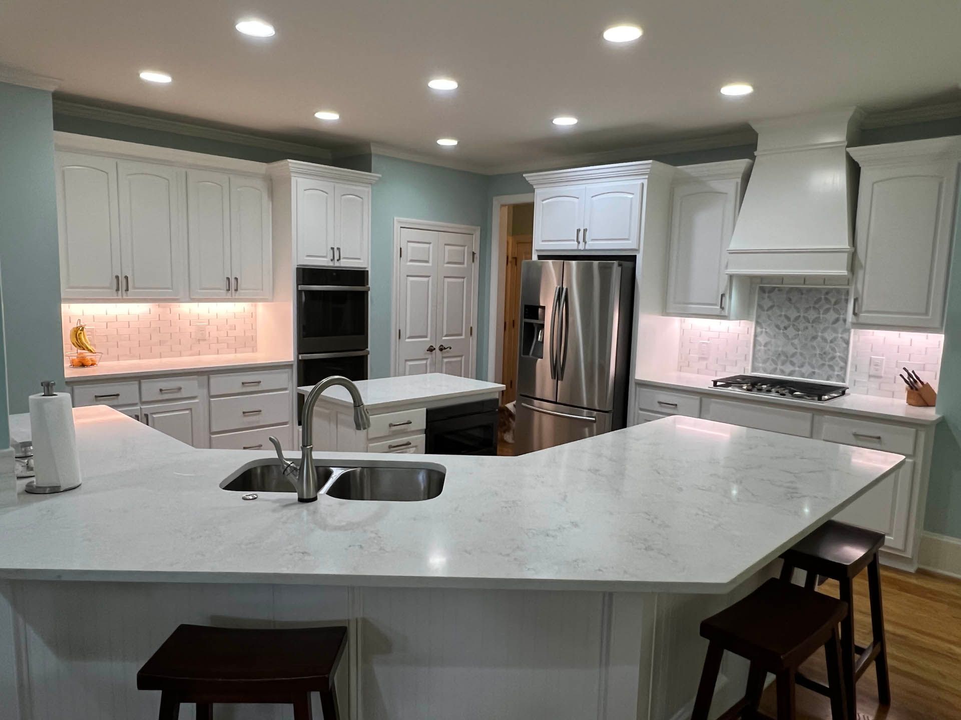 Bright, spacious kitchen with white cabinets, light blue walls, and a large island with seating. Stainless steel appliances and quartz countertops.