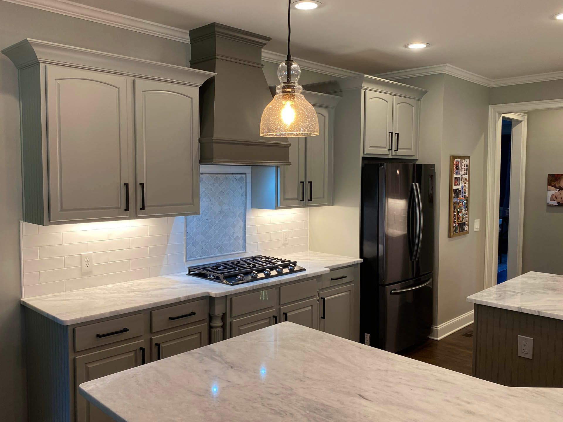 A kitchen with gray cabinets, white countertops, and a dark gray refrigerator. A pendant light hangs above the stove.