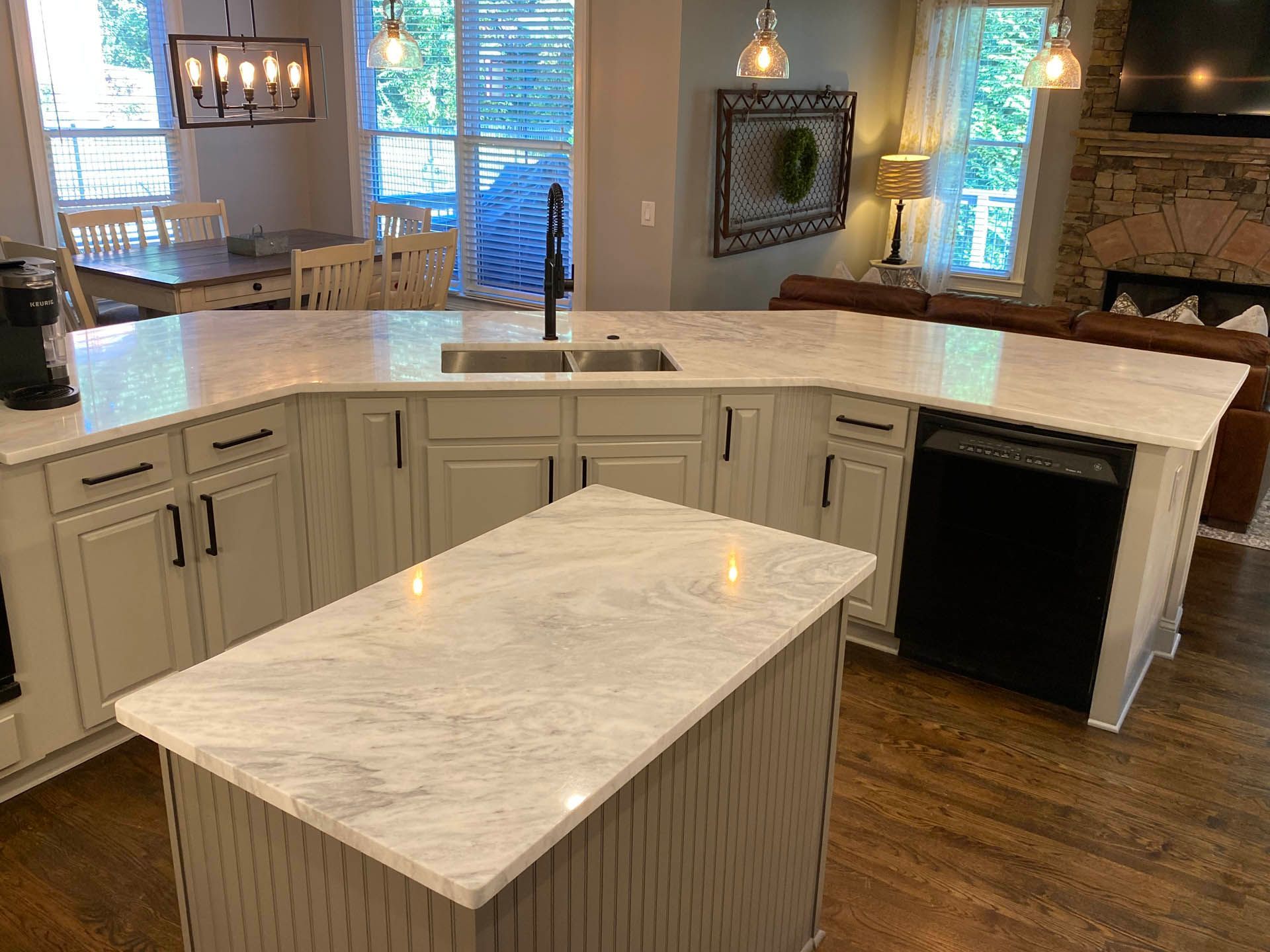 Modern kitchen with a large island and wraparound countertop. Cream-colored cabinets with black hardware, light countertops, and a black dishwasher.
