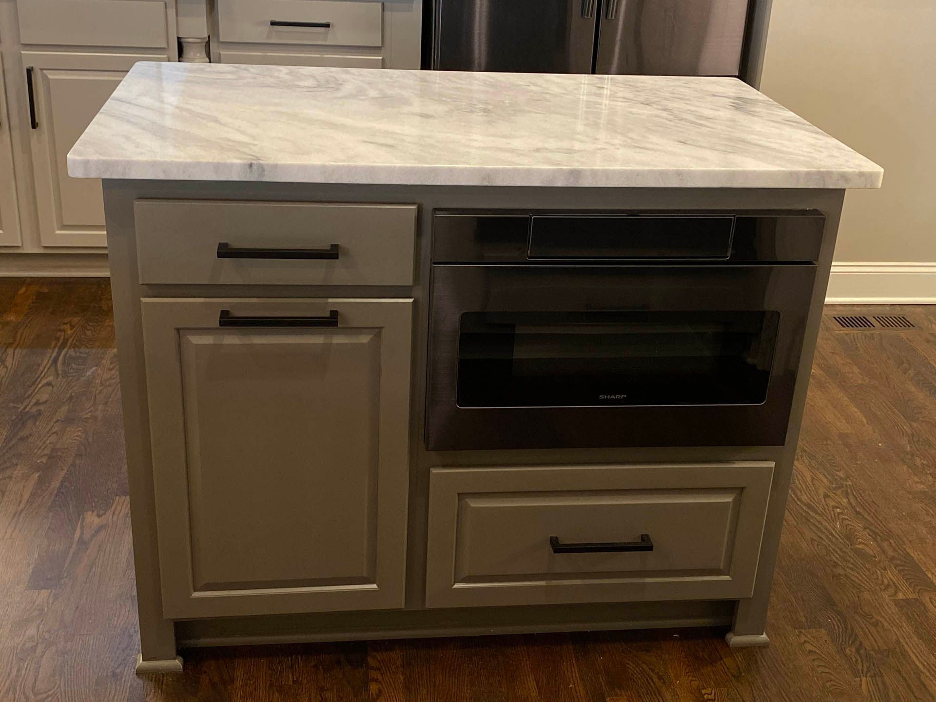 Gray kitchen island with a marble countertop, featuring cabinets, drawers, and a built-in microwave.