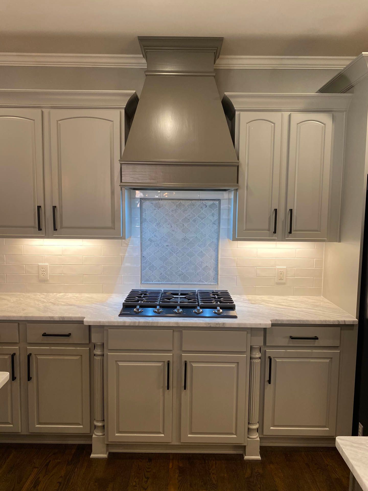 Kitchen with light gray cabinets, a stove with blue flames, and a range hood. White backsplash and dark hardware.