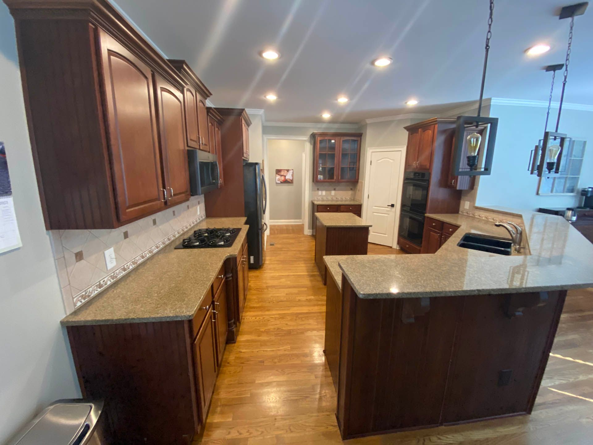 A kitchen with dark wood cabinets, granite countertops, and a central island. Includes appliances, recessed lighting, and hardwood floors.