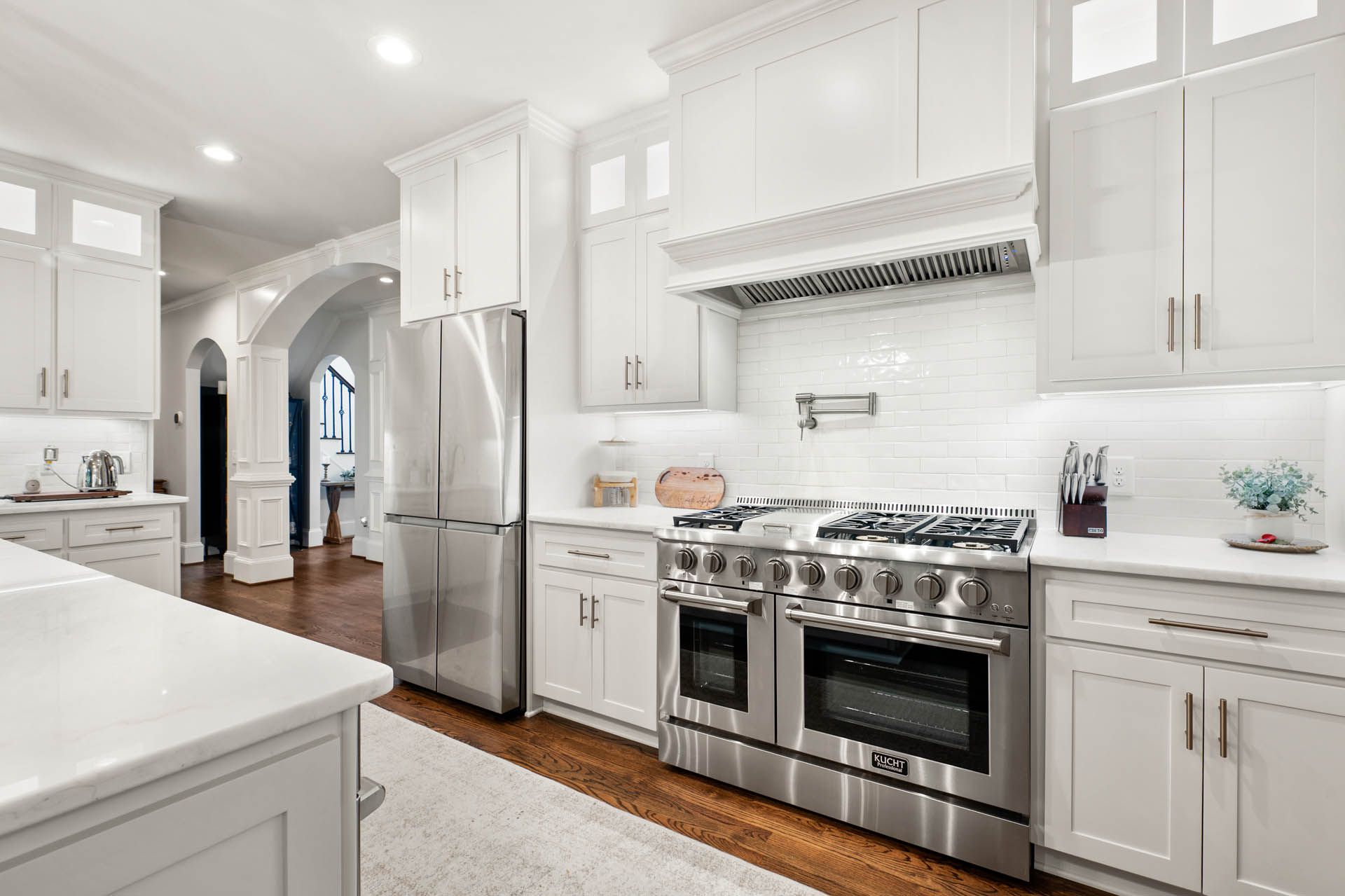 Modern white kitchen with stainless steel appliances, white cabinetry, and a gas range. An arched doorway leads to another room.