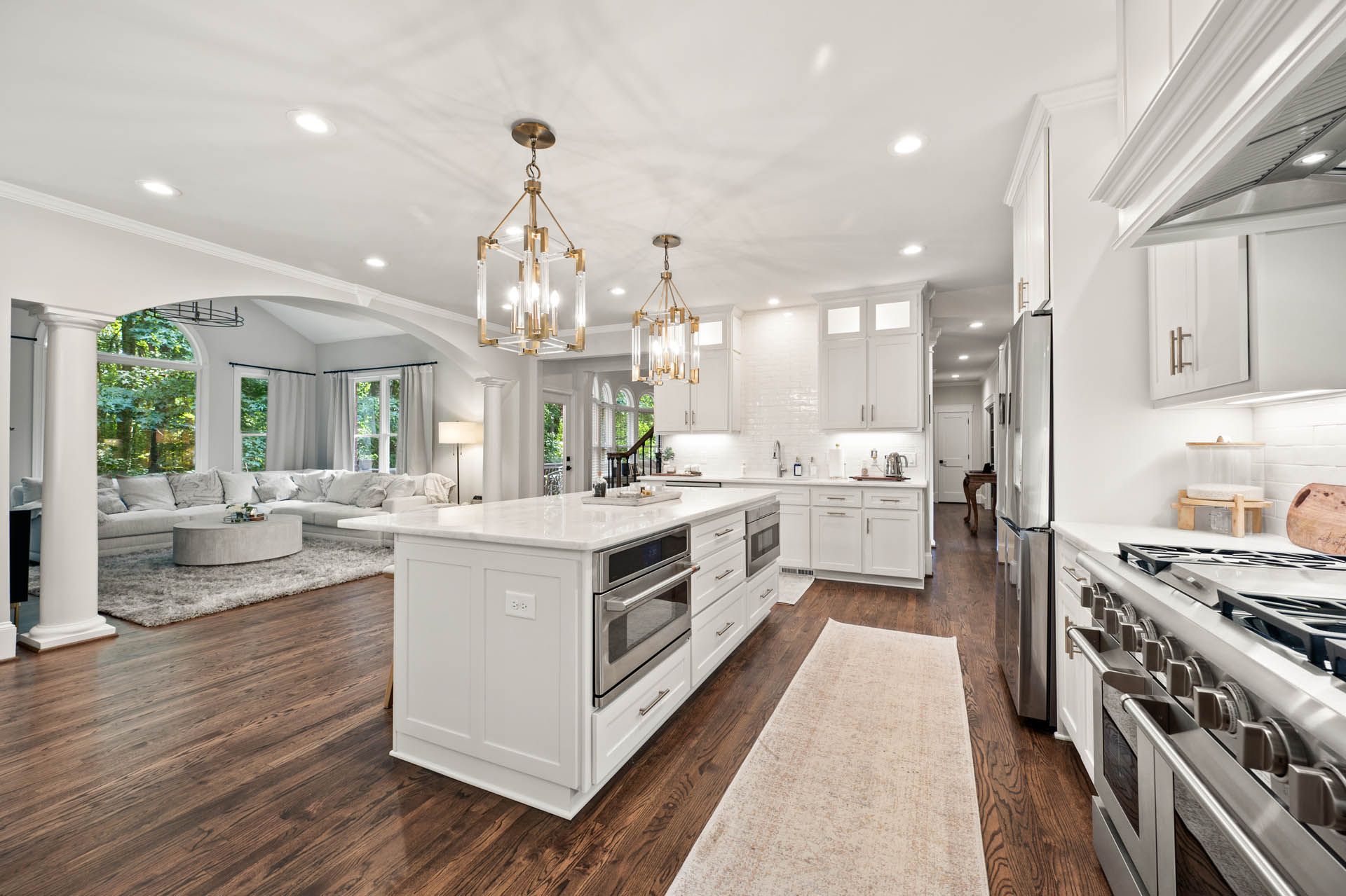 Spacious, bright kitchen with a white island and cabinets, open to a living room with hardwood floors and a view of the outdoors.