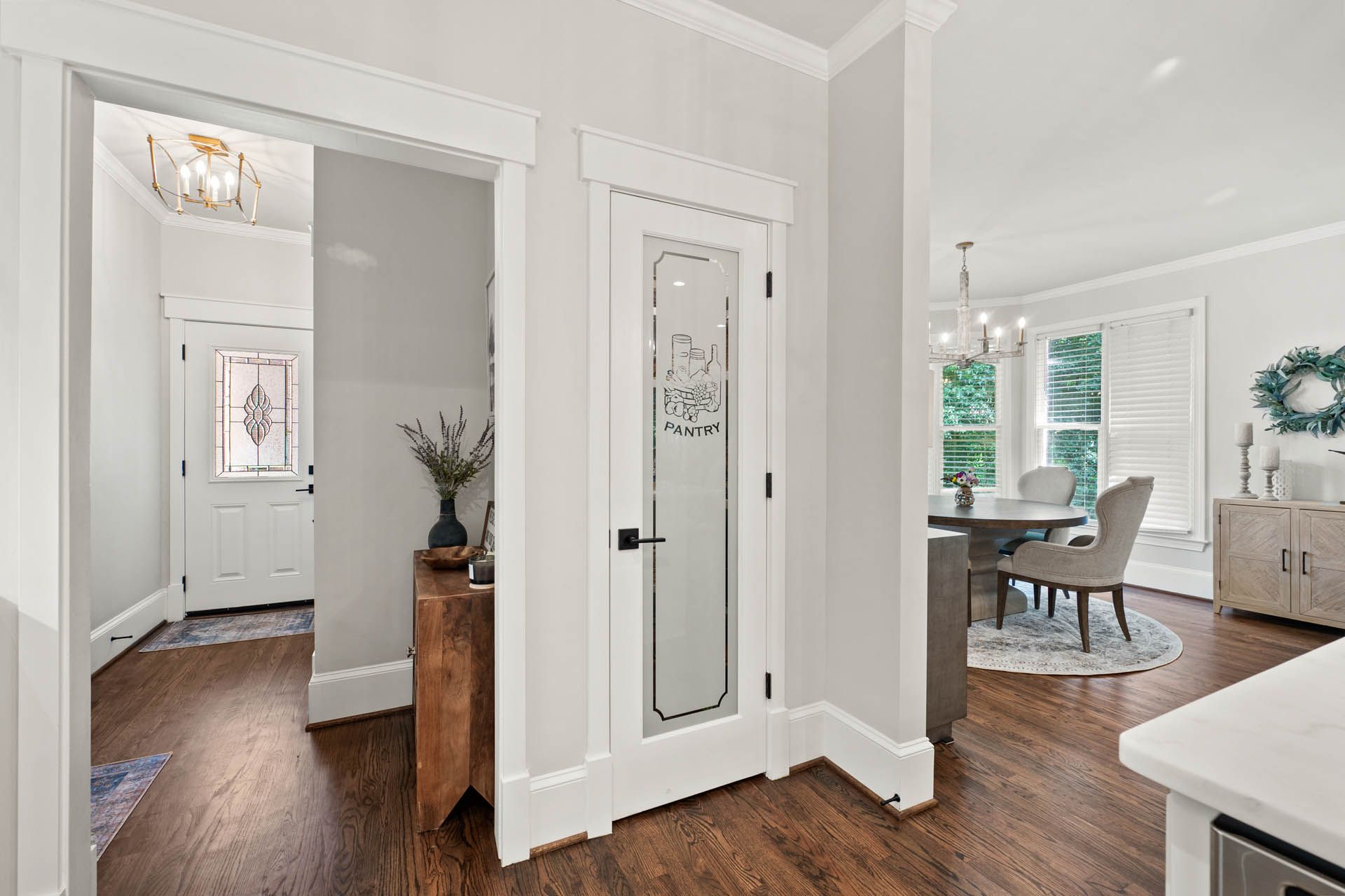 Entryway with dark wood floors, a pantry with etched glass, and a view into a dining room with a round table.